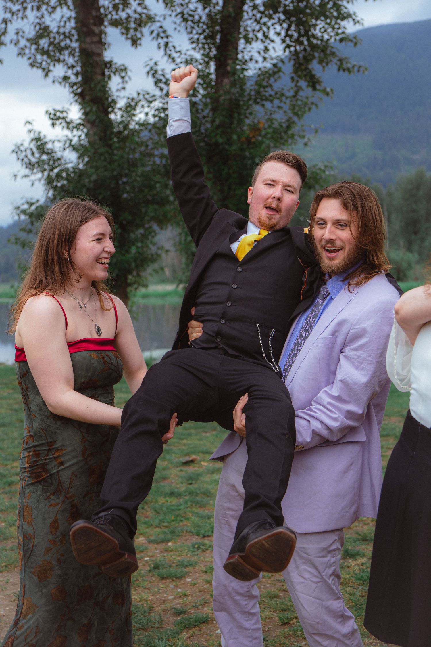 Groom lifted by friends in celebration at an outdoor mountain wedding reception.