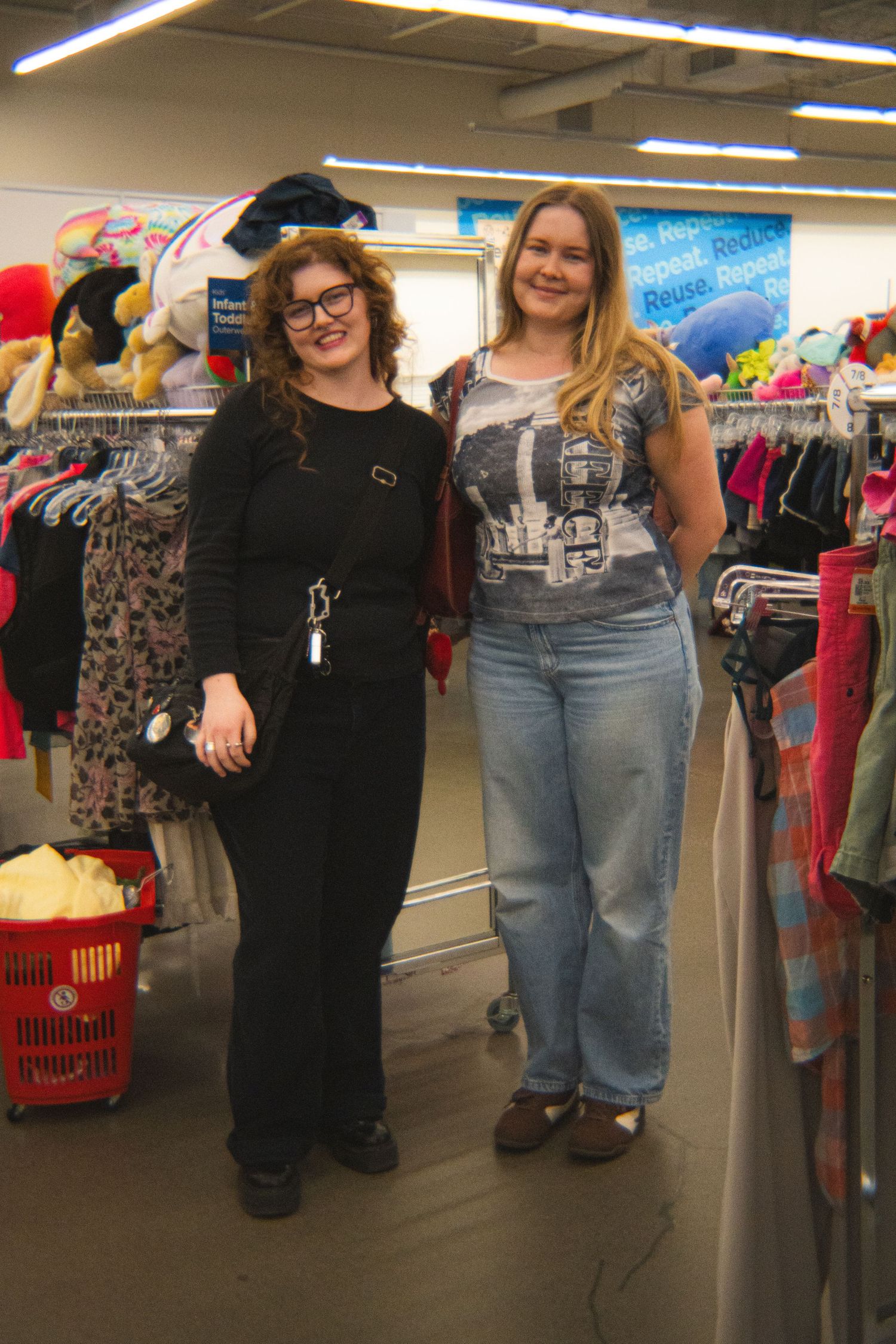 Two women smiling together while thrift shopping in a secondhand clothing store.