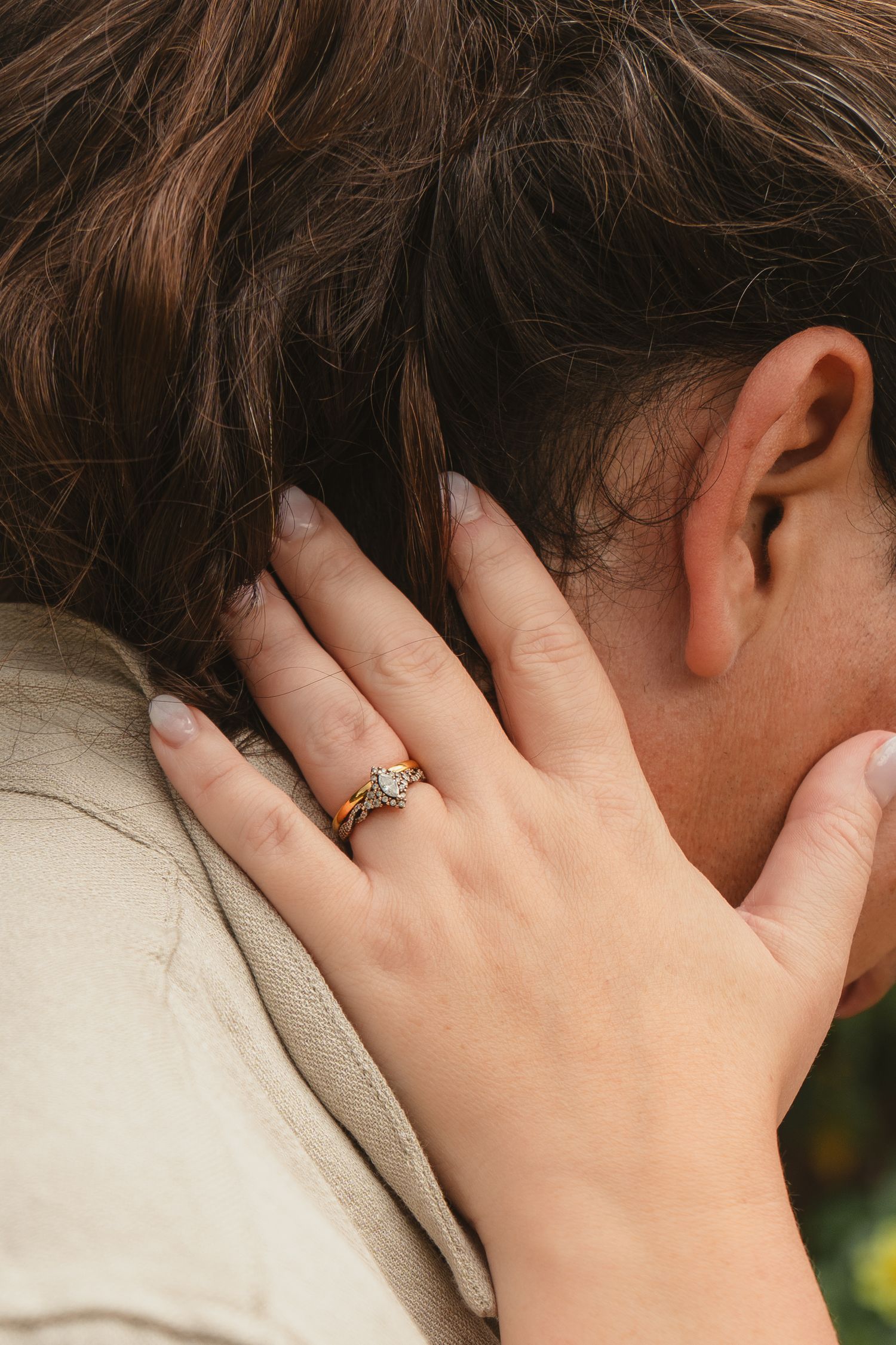 Close-up of a woman's hand with a gold diamond engagement ring resting on a man's shoulder during an embrace.
