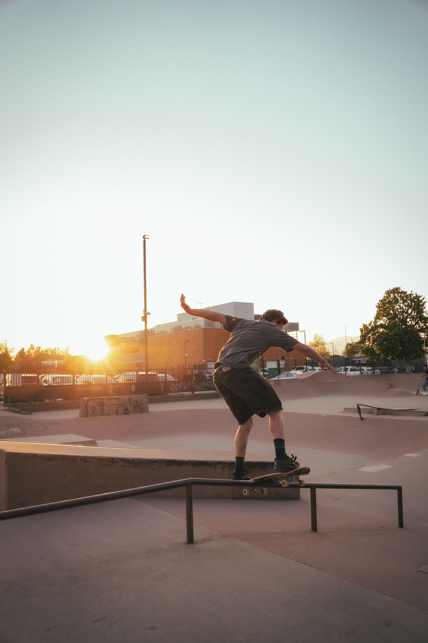 Skateboarder grinding a rail at an outdoor skate park during a vibrant golden hour sunset.