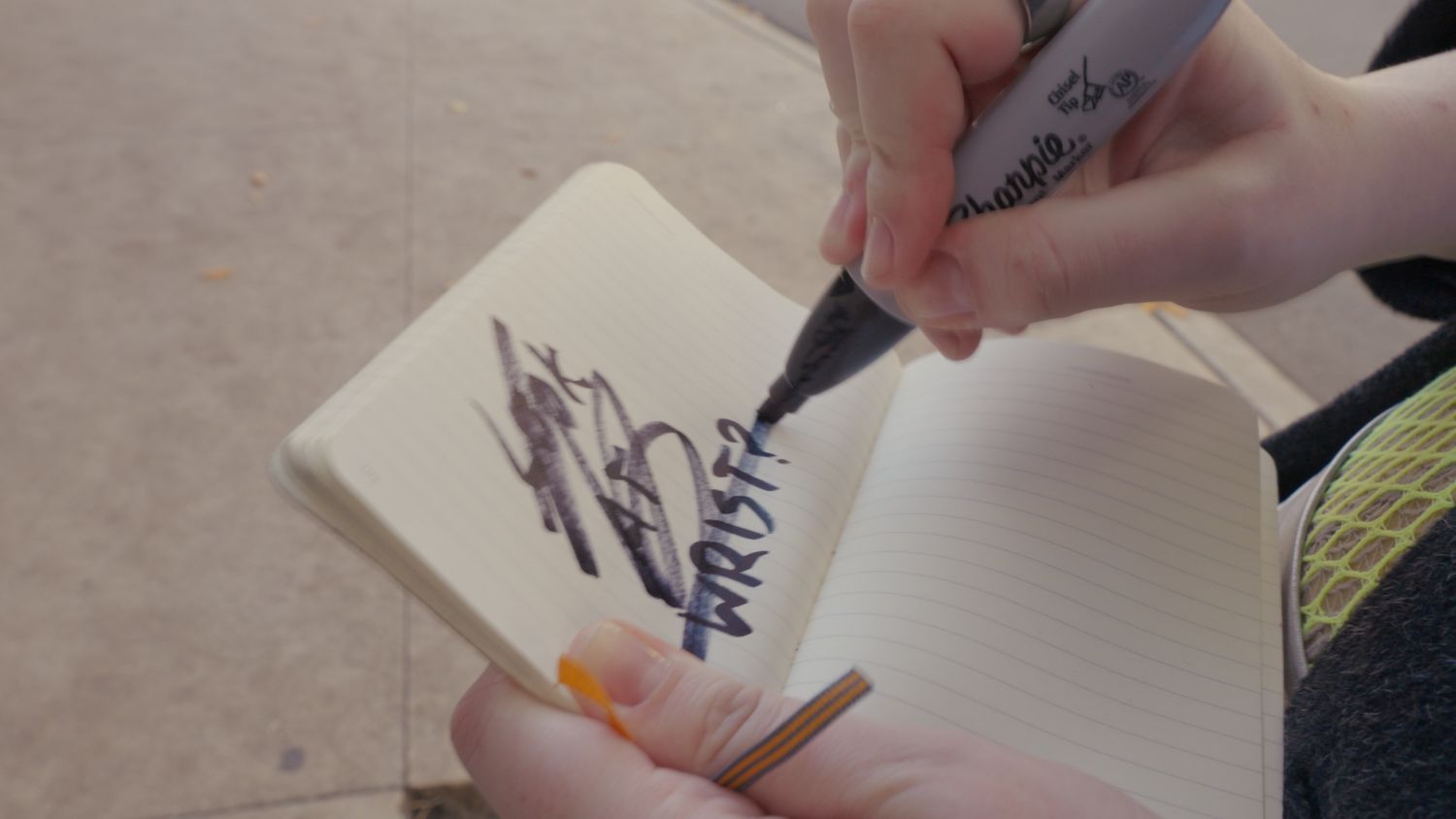 Close-up of hands writing the word trust in stylized lettering on a small notebook with a marker.