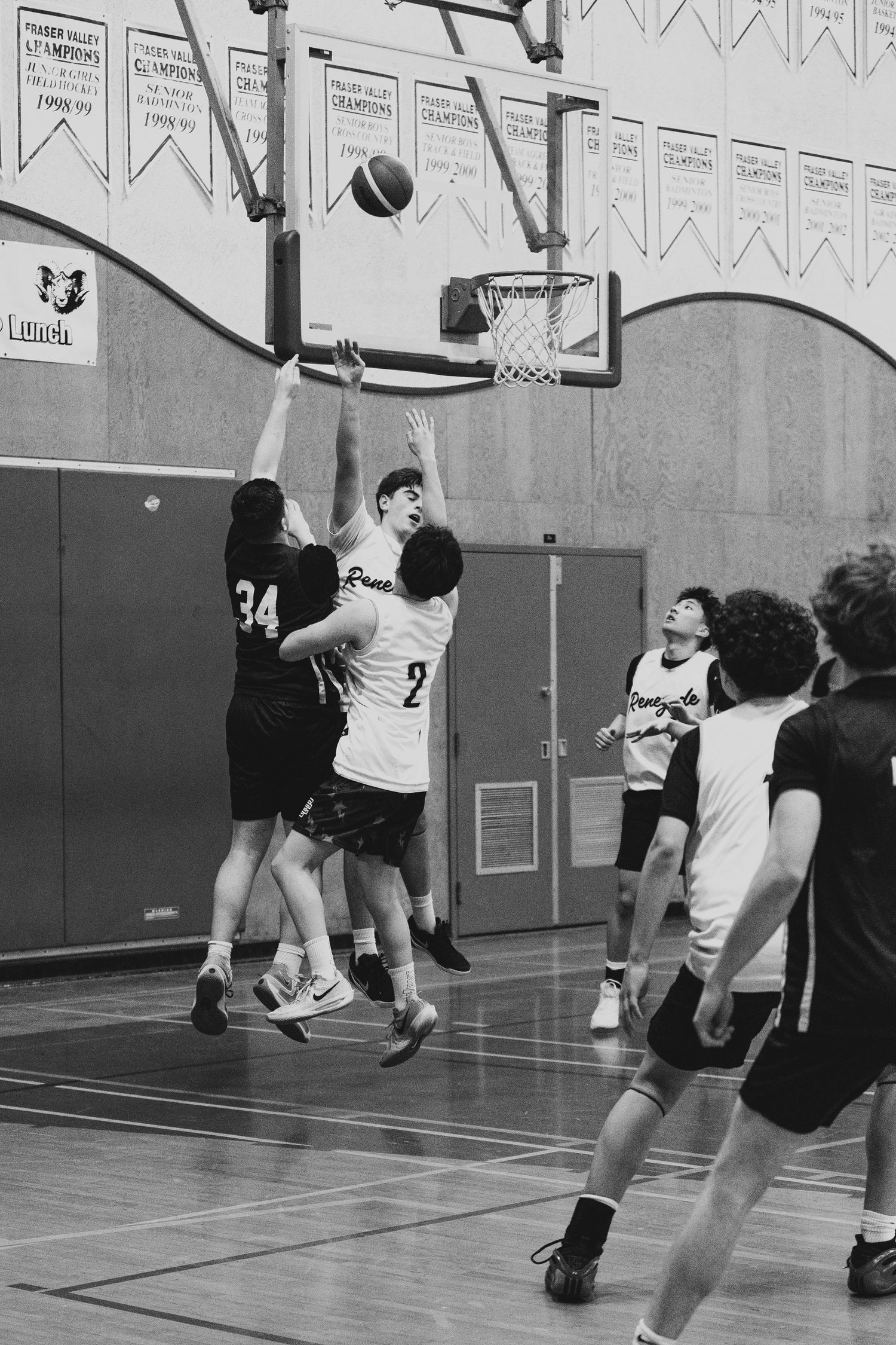 Black and white photo of a basketball player in white jersey blocking a shot near the hoop.