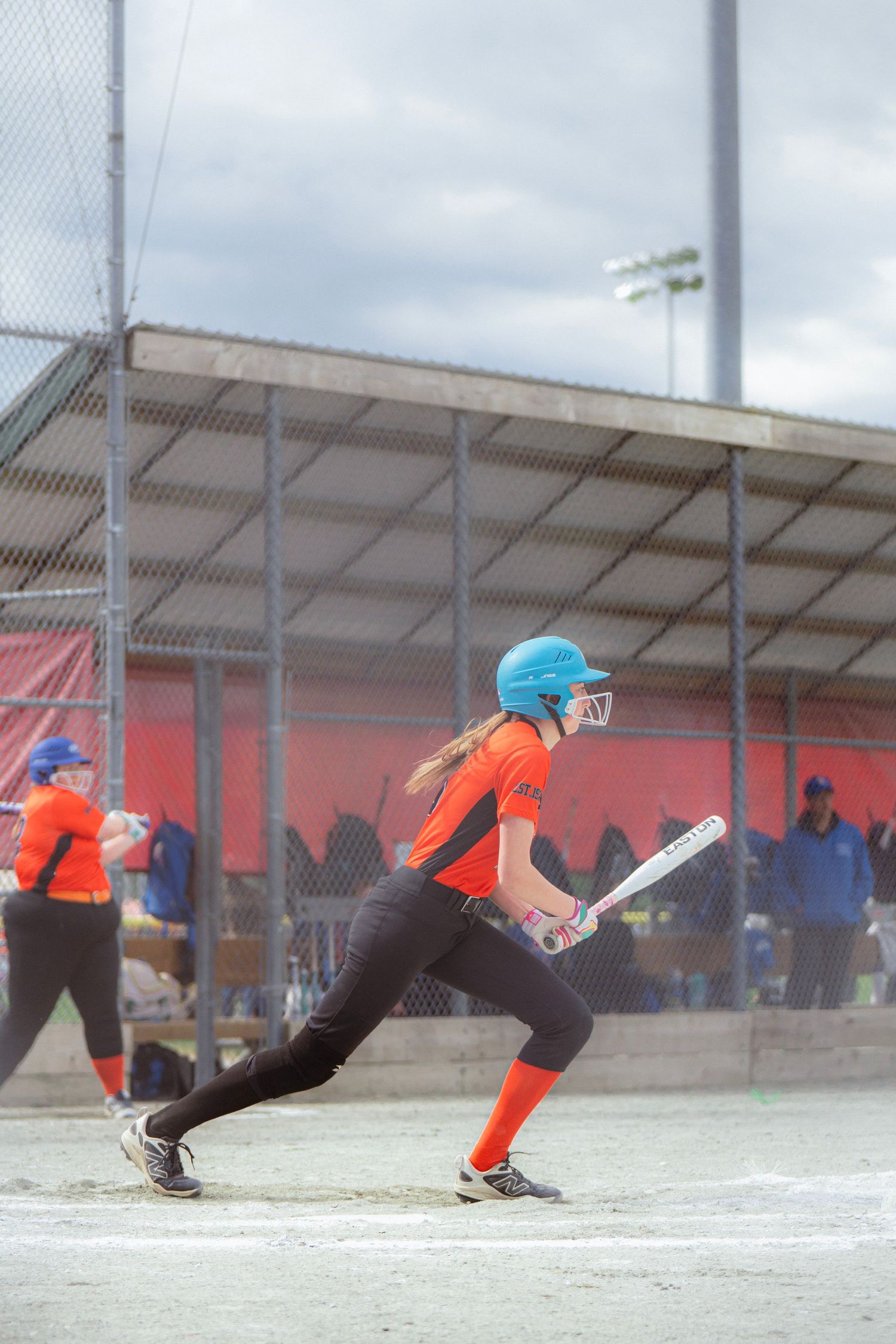 Female softball player in orange uniform swinging bat at home plate during a game.