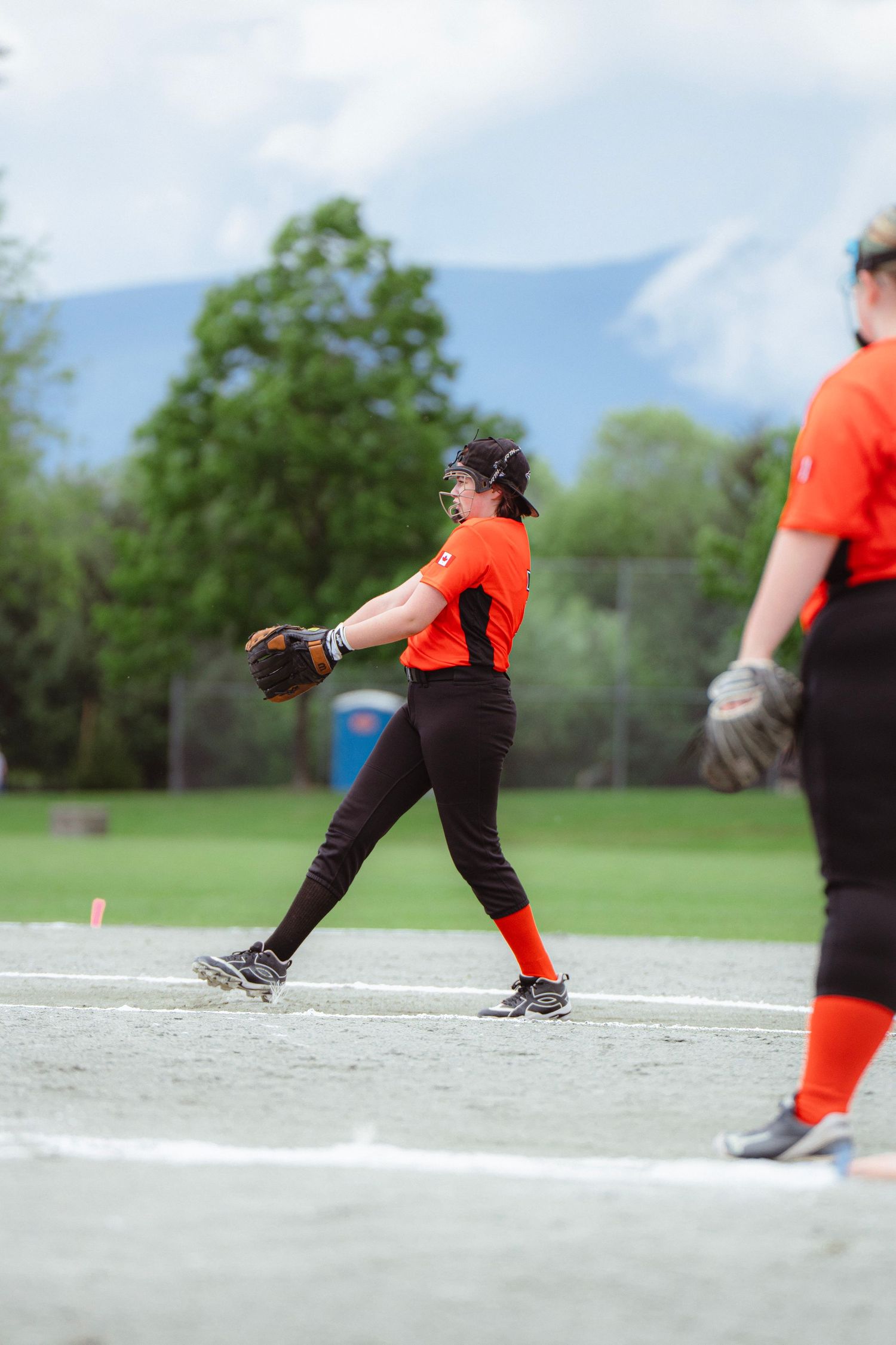 Female softball player in orange uniform fields a ball on the diamond during an outdoor game.