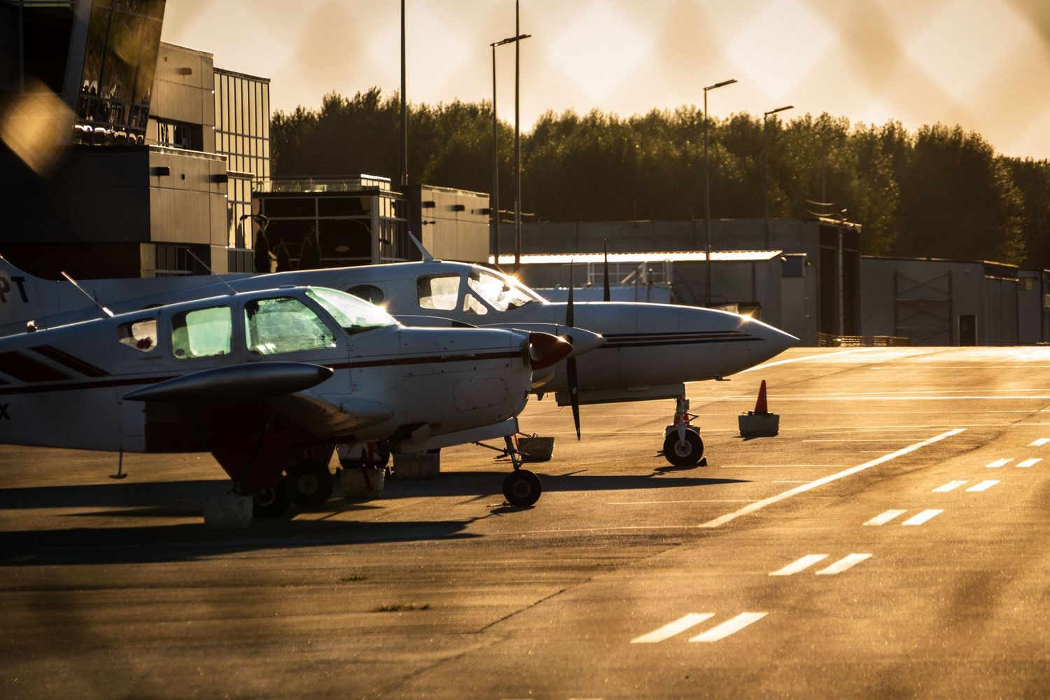 A twin-engine propeller plane parked on a sunlit airport tarmac during golden hour.