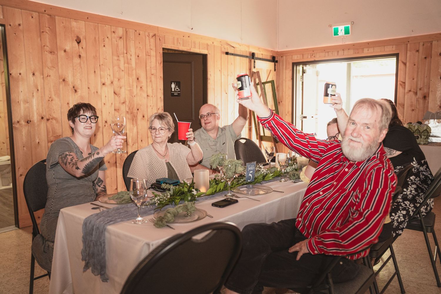 Group of seniors raising glasses in a toast at a decorated dining table in a wood-paneled room.
