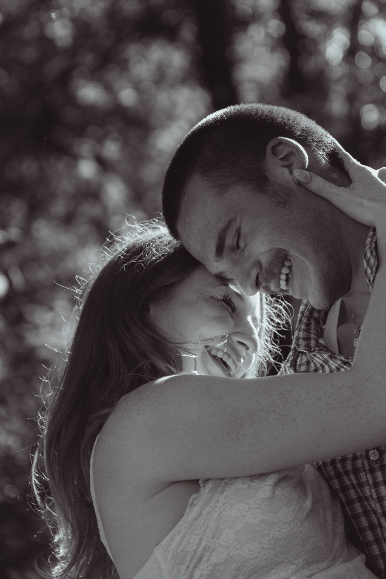 Black and white photo of a happy couple embracing and laughing together outdoors among trees.