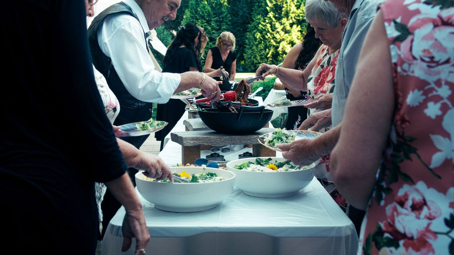 Guests serving themselves fresh salads at an outdoor wedding reception buffet table.