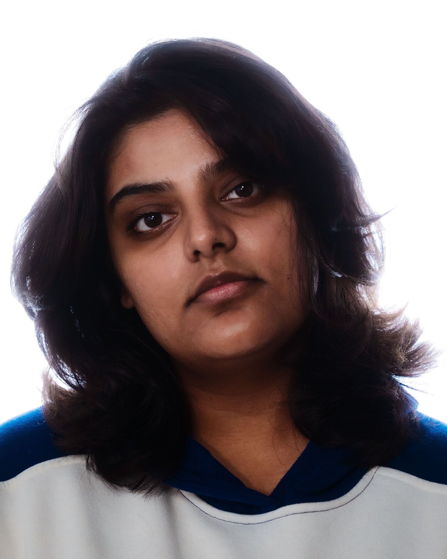 Young woman with dark wavy hair wearing a blue and white jersey, close-up portrait on white background.