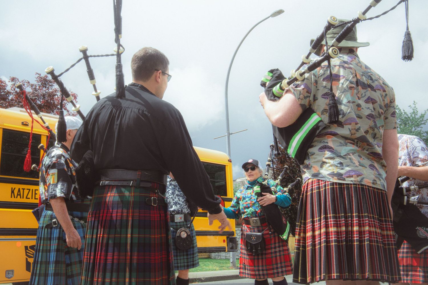 Bagpipers in traditional kilts prepare to march near a yellow school bus at an outdoor event.