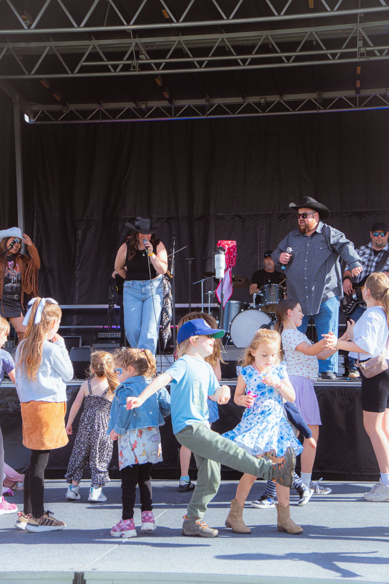 Children dancing in front of an outdoor stage with country band performers at a festival.