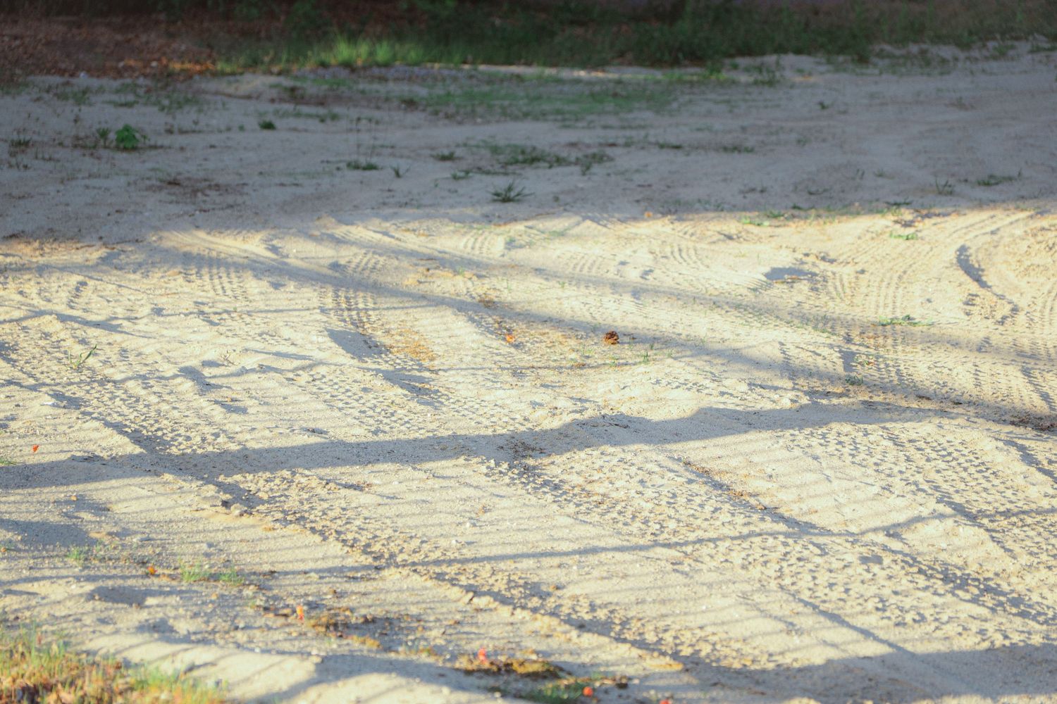 Sandy ground covered with overlapping tire tracks and shadows in golden afternoon light.