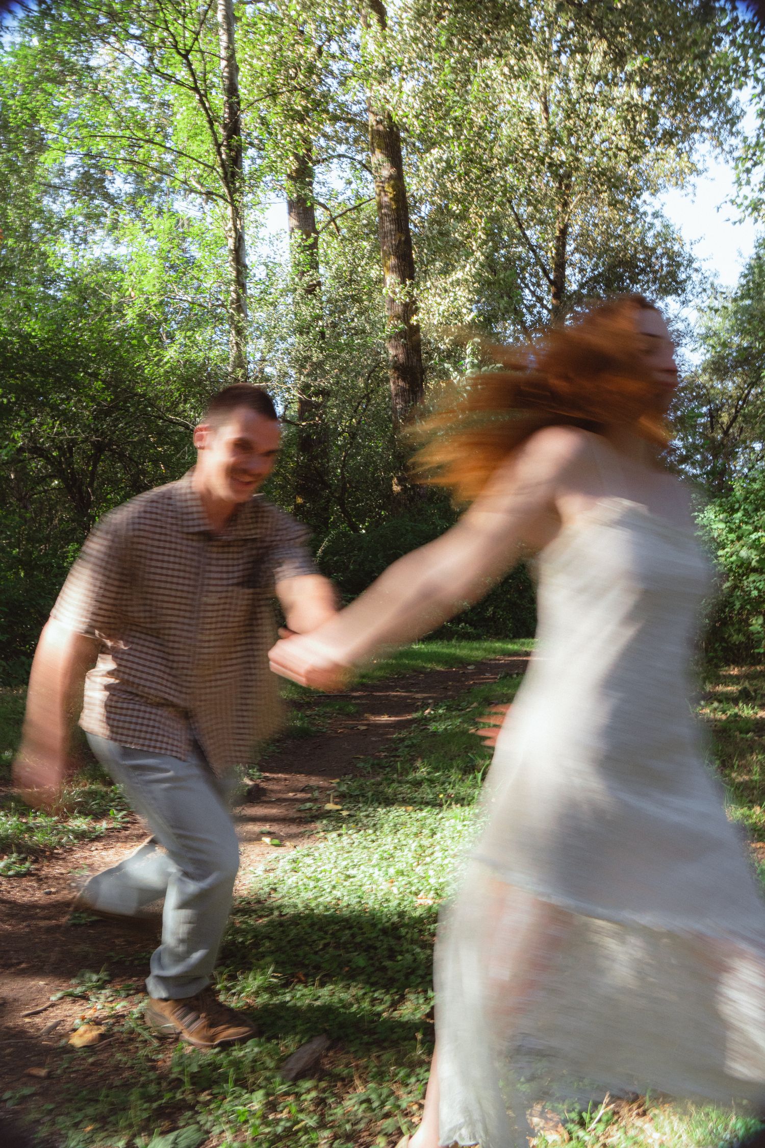 Couple dancing joyfully in a sunlit forest park, motion blur capturing their energetic spin on a green woodland path.