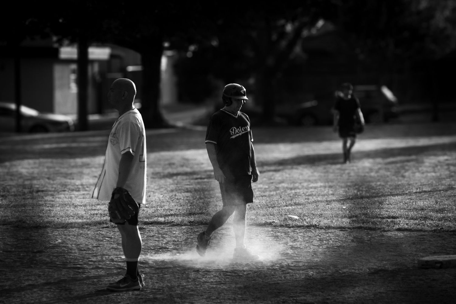 Black and white photo of baseball players on a dusty field in evening light.