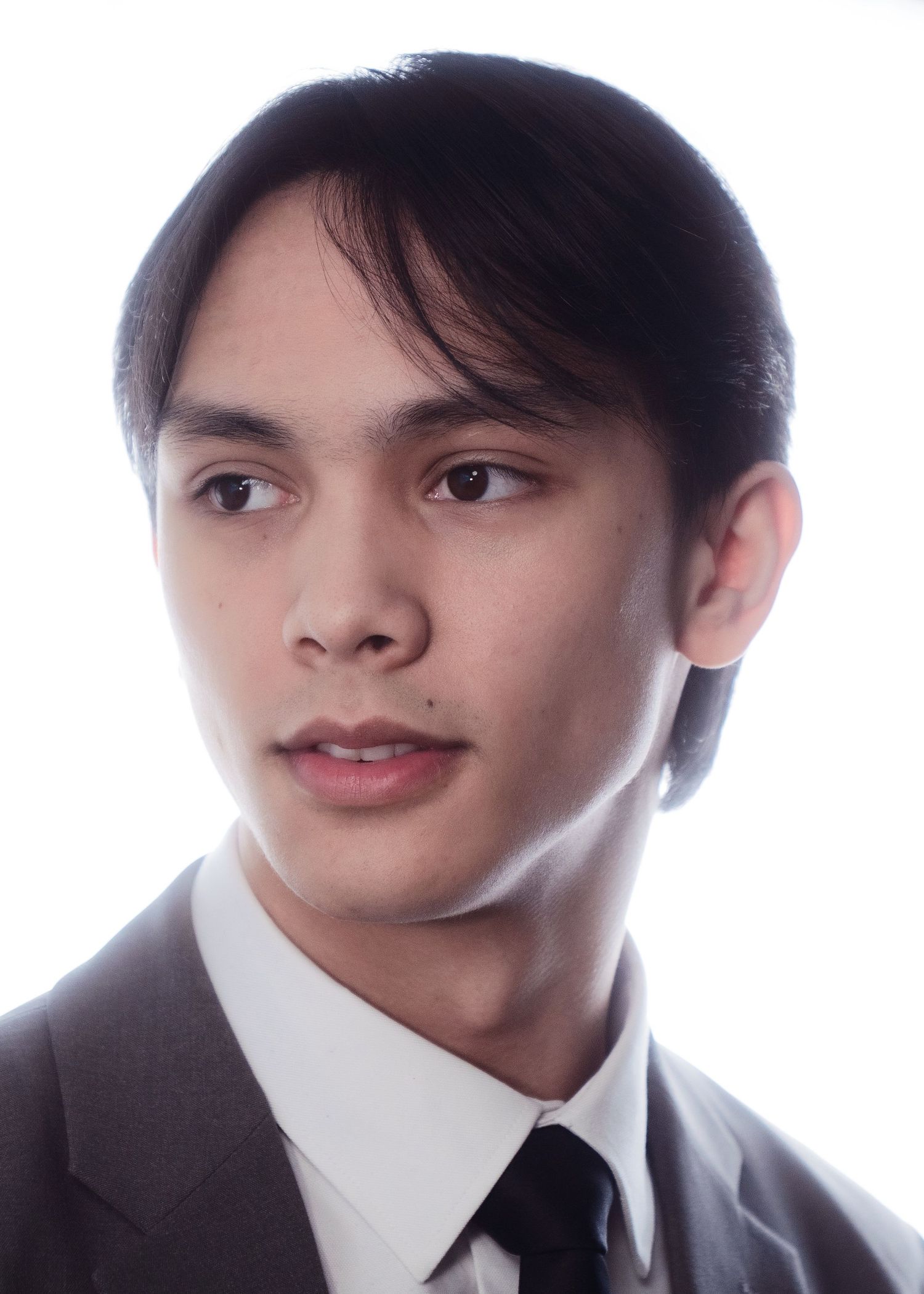 Young man with dark side-swept hair in a suit and black tie, professional headshot on white background.