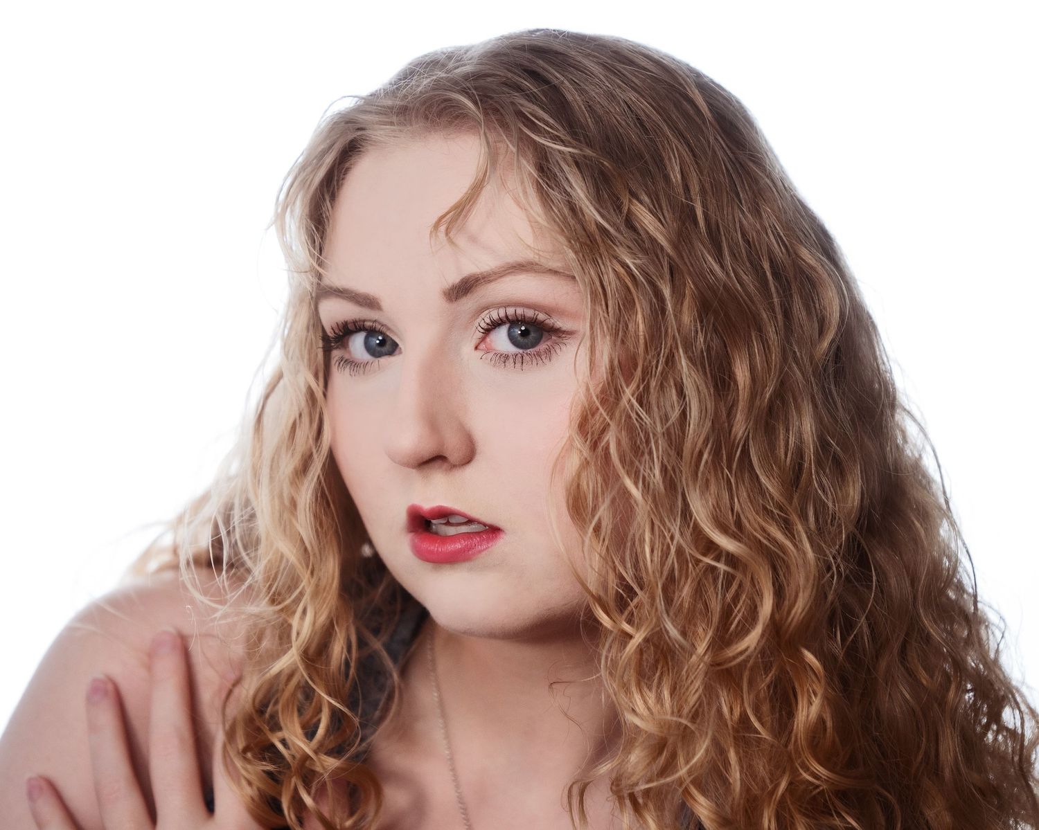 Young woman with curly blonde hair and blue eyes wearing a pink top against white background.