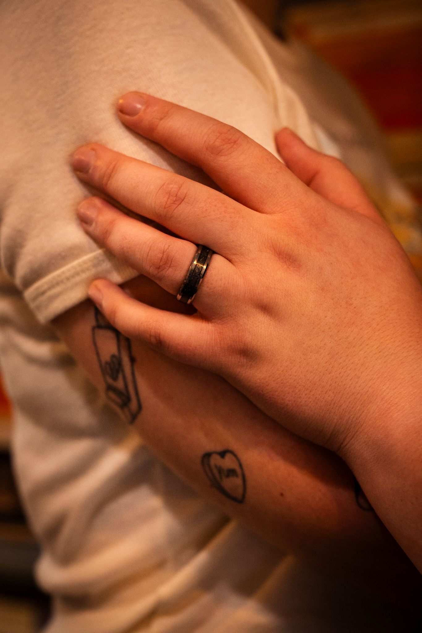 Close-up of a hand with a black ring resting on a white shirt sleeve, with small tattoos visible.