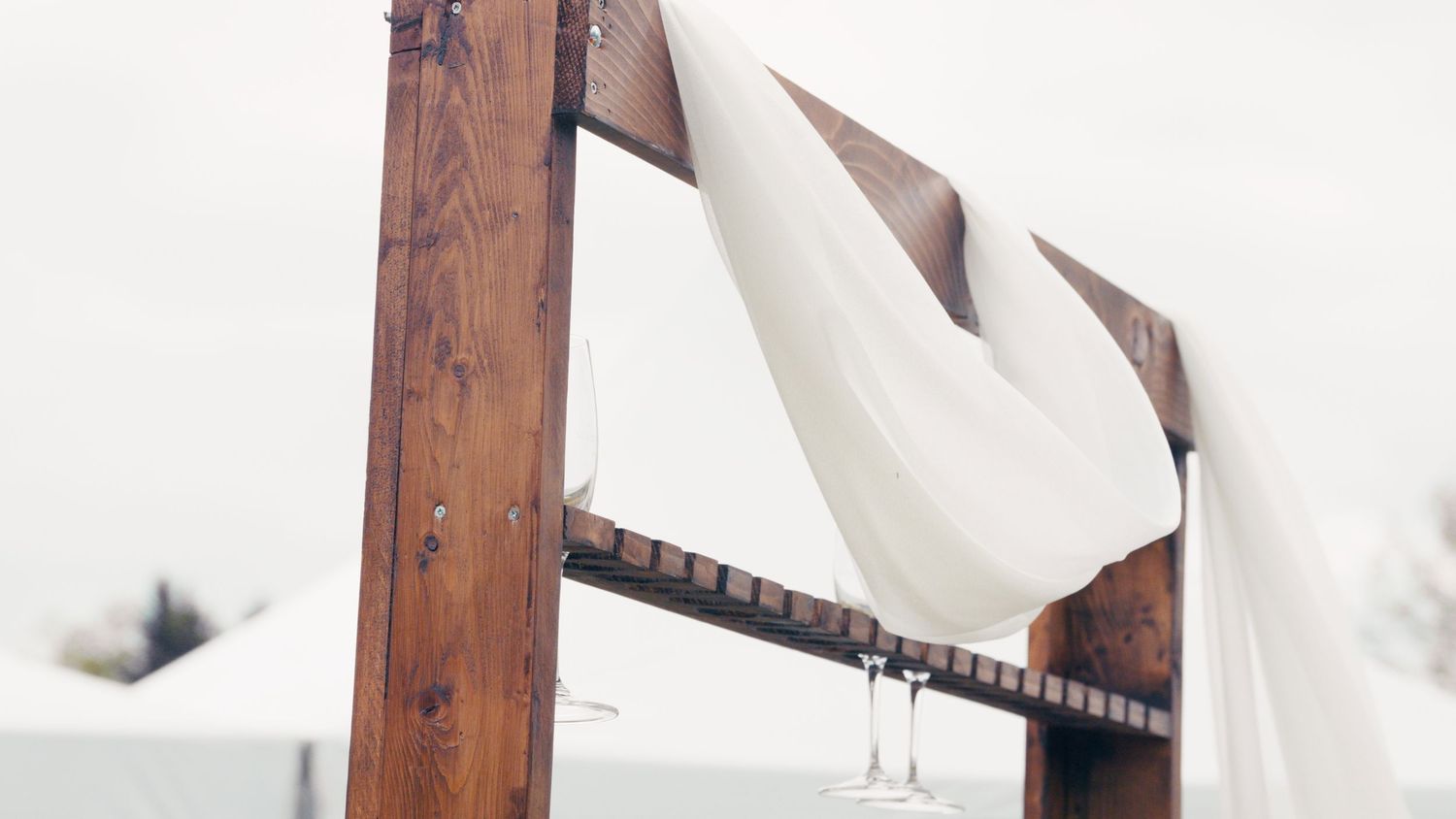 Rustic wooden wedding arch adorned with flowing white fabric draped elegantly outdoors.