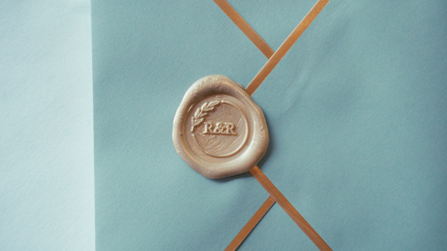 Elegant gold wax seal with RER monogram on light blue envelope with ribbon detail.