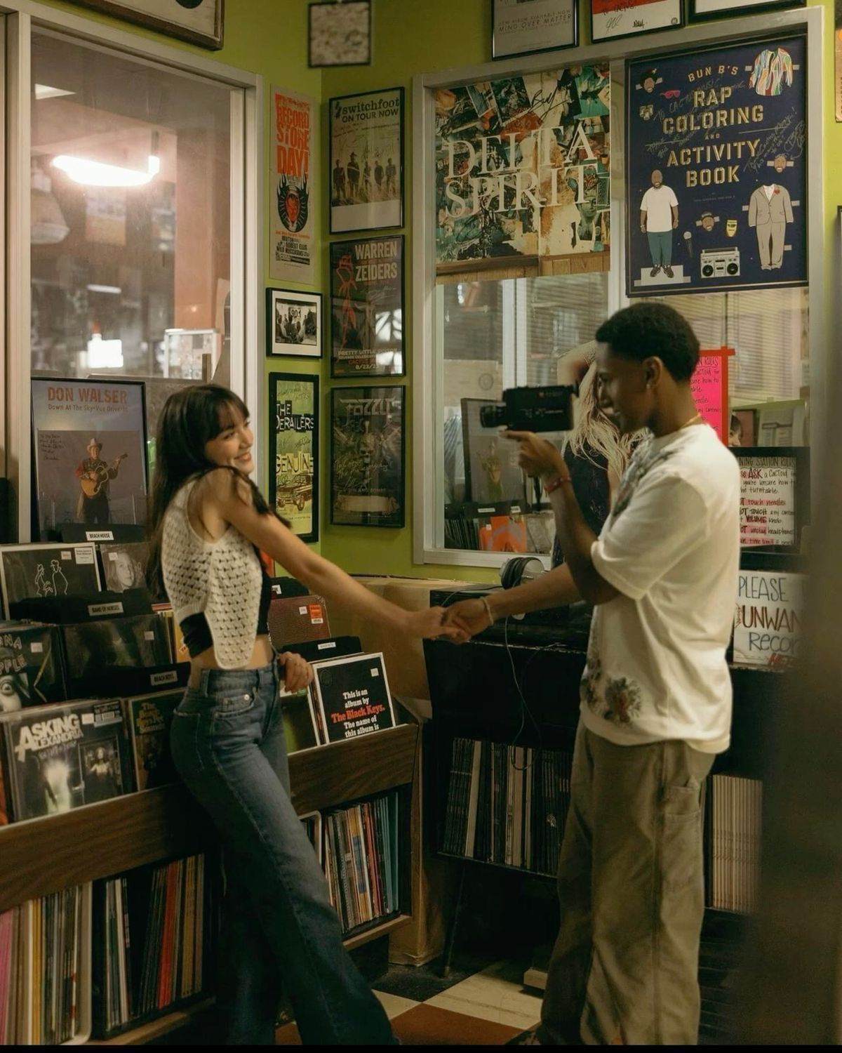 Two people dancing and holding hands in a vinyl record shop surrounded by music posters and album covers.
