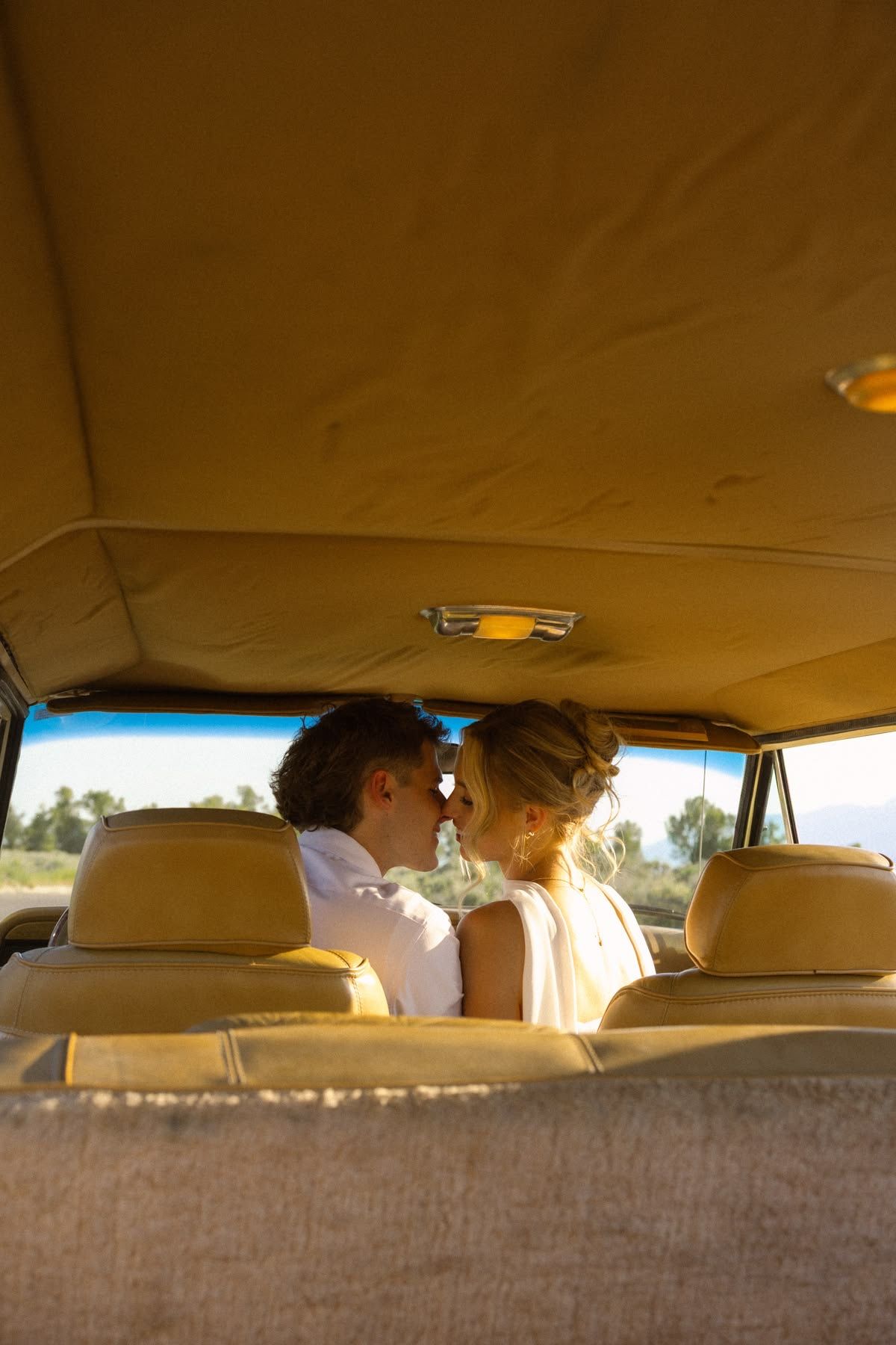 Couple sharing a romantic moment in the backseat of a vintage car with tan leather interior.
