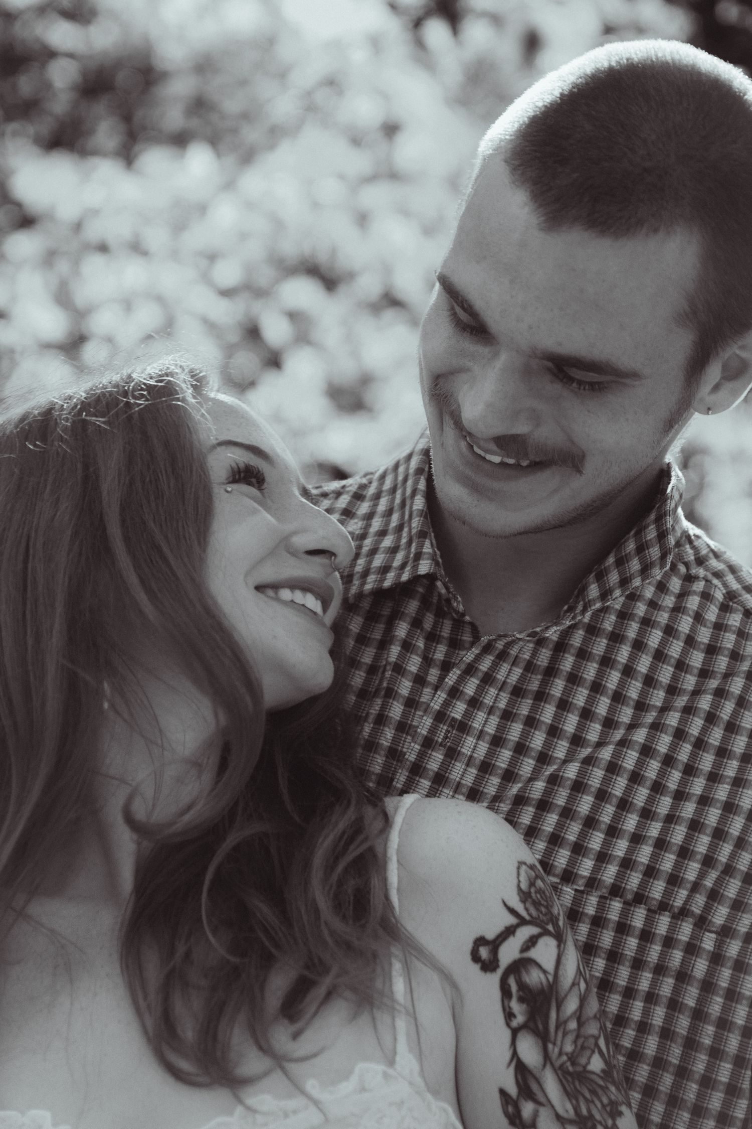 Black and white portrait of smiling couple gazing at each other tenderly outdoors.