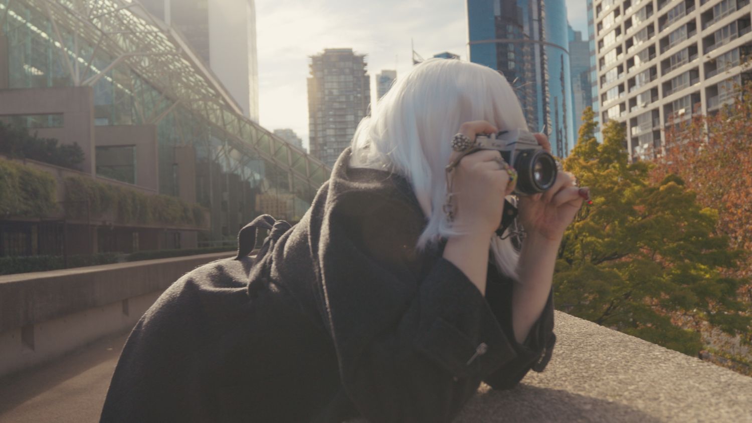 Woman with white hair photographing with film camera in urban cityscape.