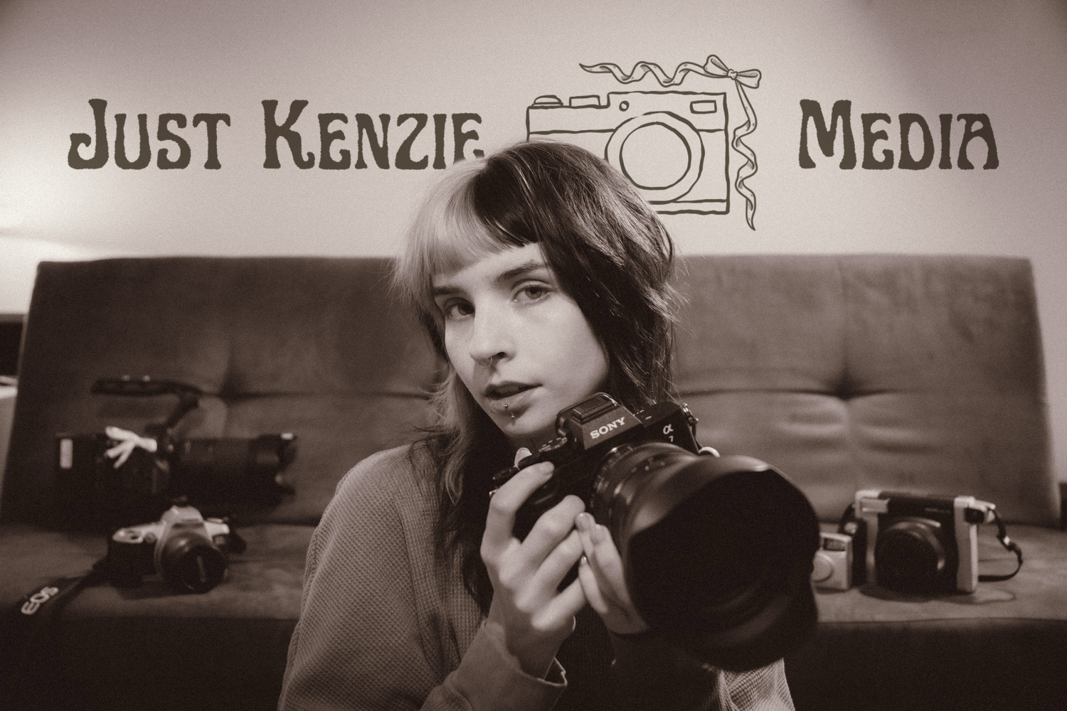 Young photographer holding a camera at Just Kenzie Media studio surrounded by vintage cameras in sepia tone.