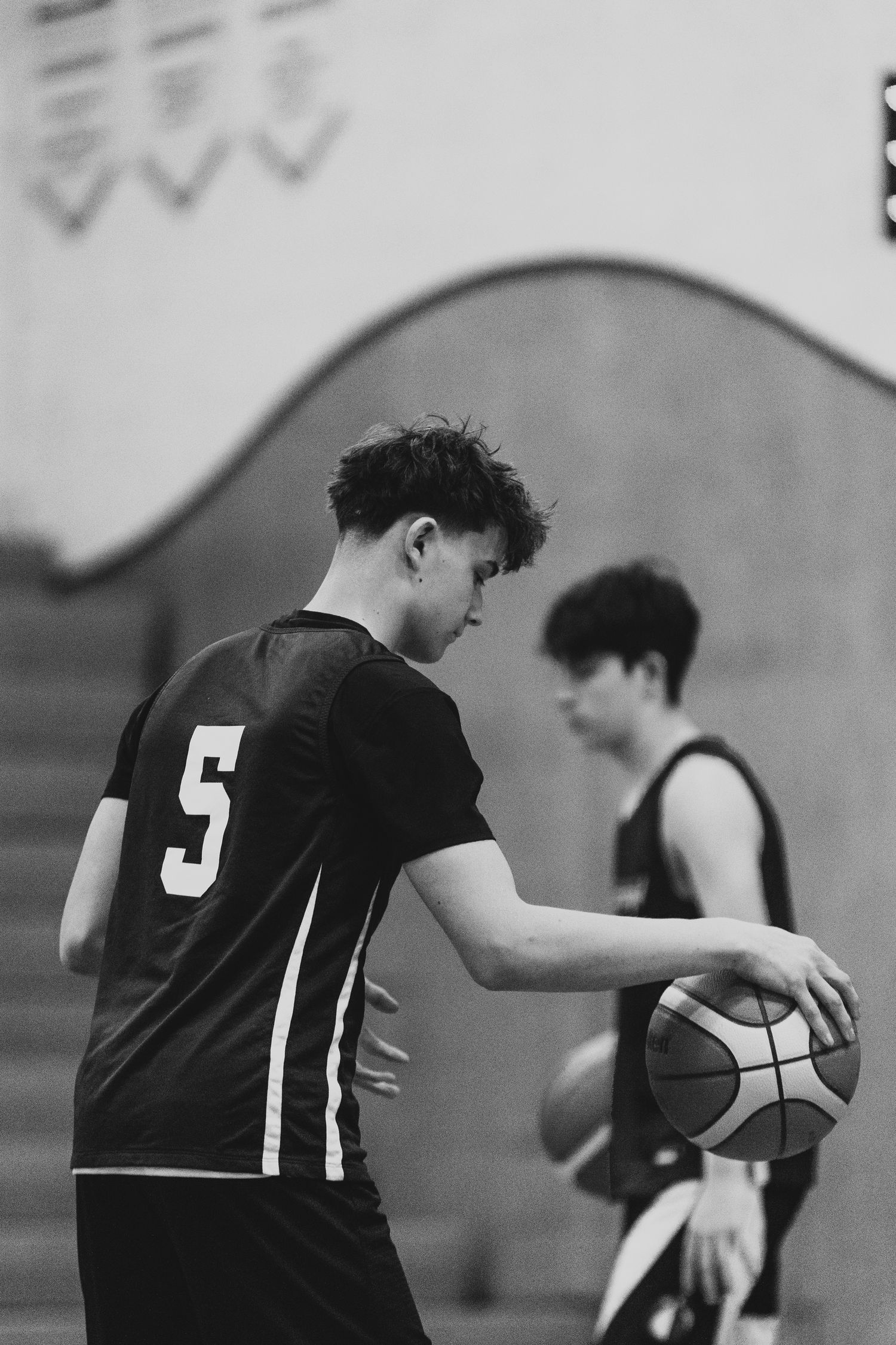 A young male basketball player wearing number 5 dribbles a ball in a black and white gym photo.