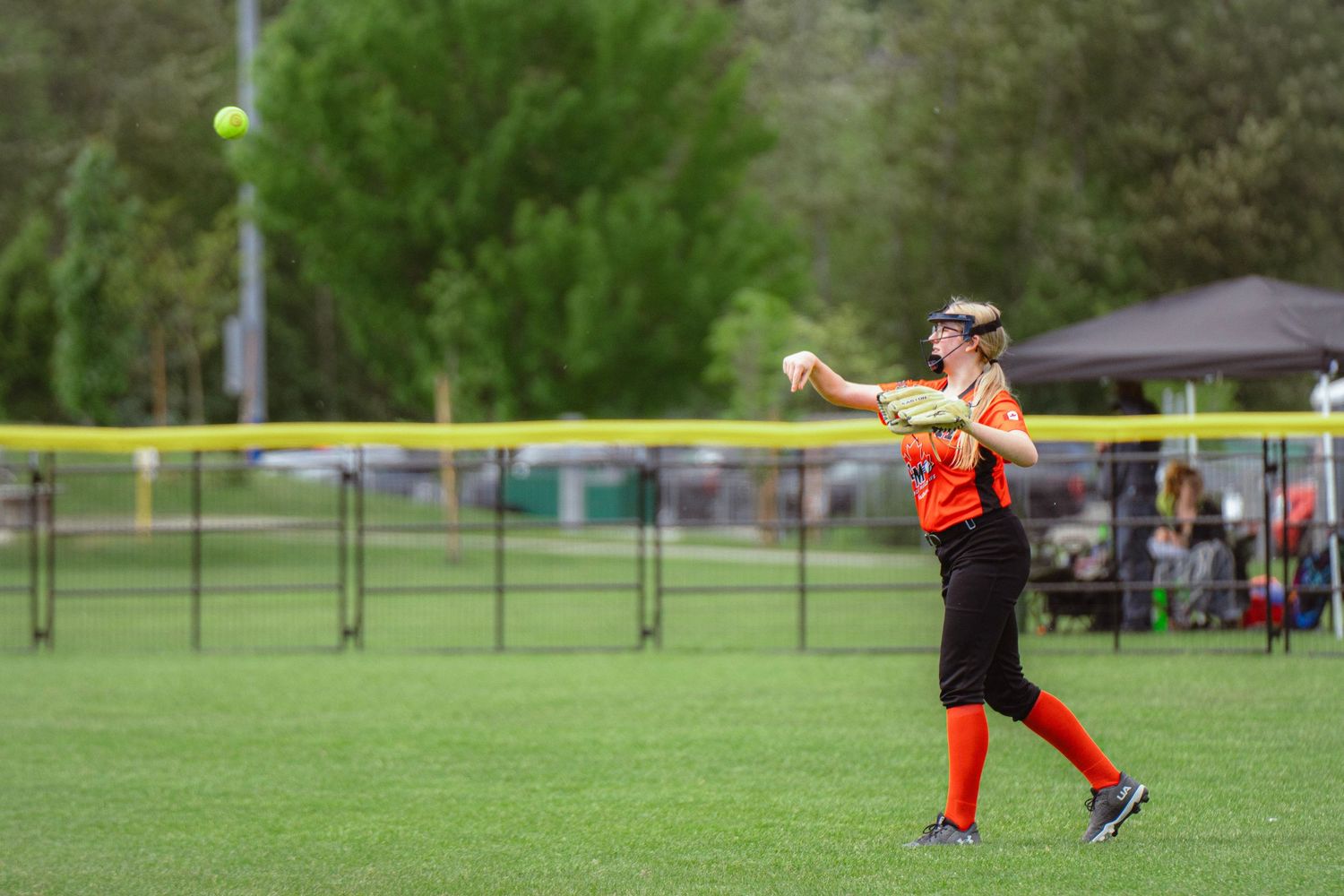 Female softball player in orange uniform throwing ball across the outfield during game.