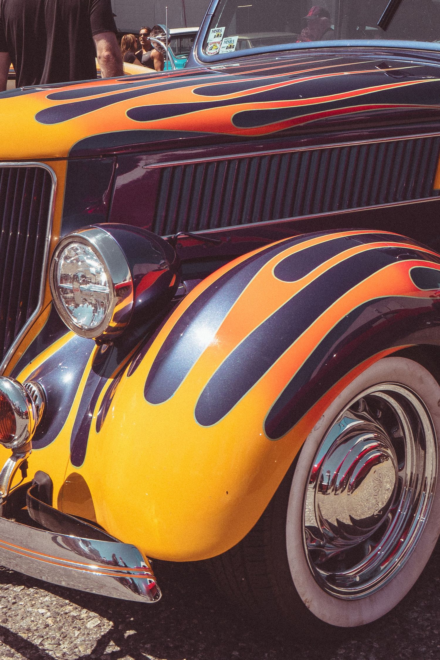 Close-up of a vintage hot rod with bold orange and black flame paint job on deep purple bodywork.
