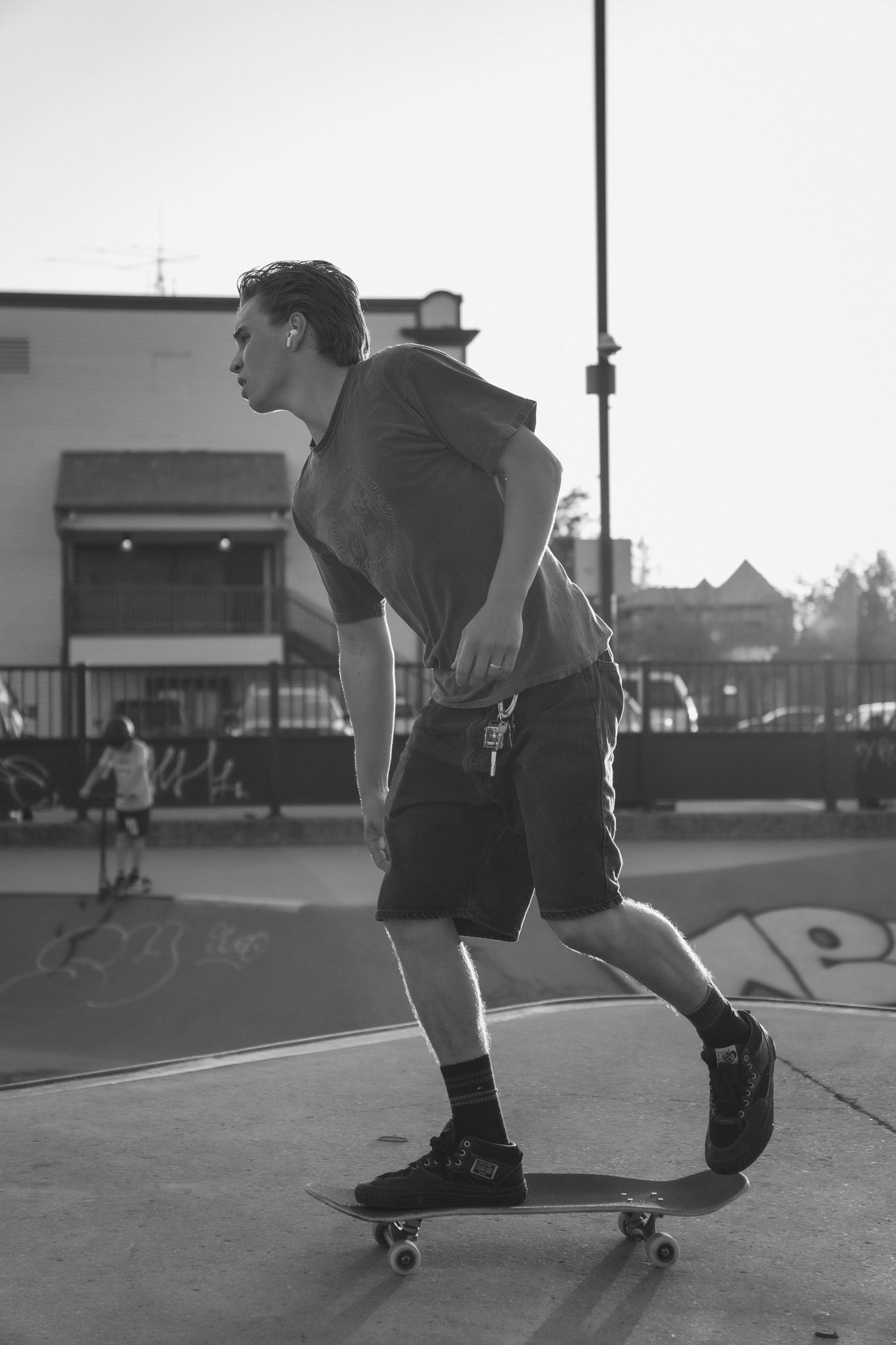 Black and white photo of a young man riding a skateboard at an outdoor skate park.