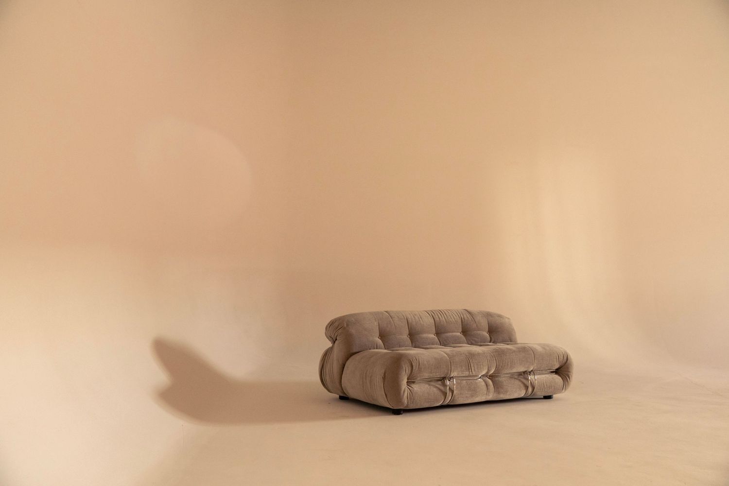 Minimalist beige studio with a single tufted sofa centered against a curved backdrop.