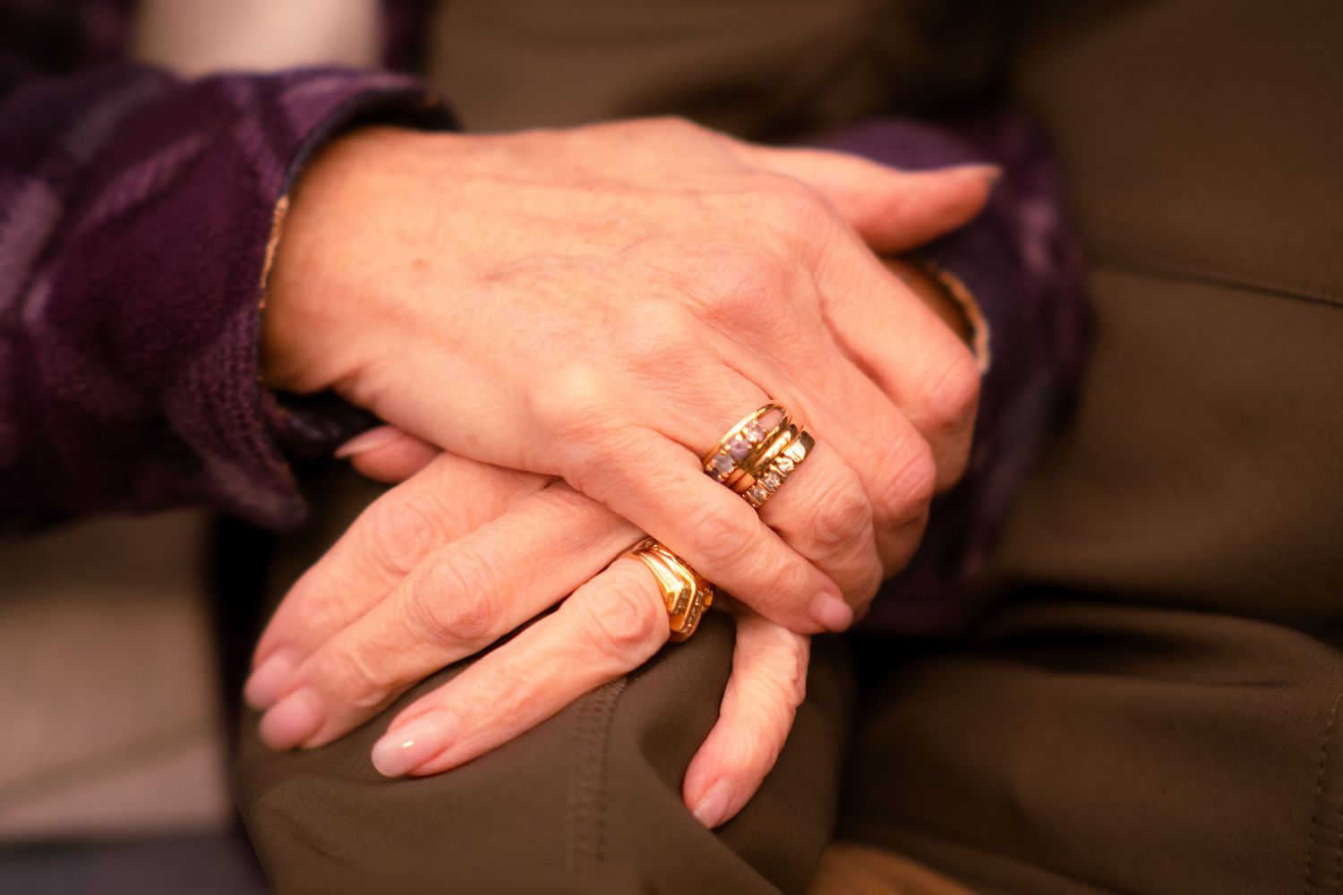 Close-up of elderly couple's clasped hands wearing gold wedding rings, symbolizing lasting love and commitment.