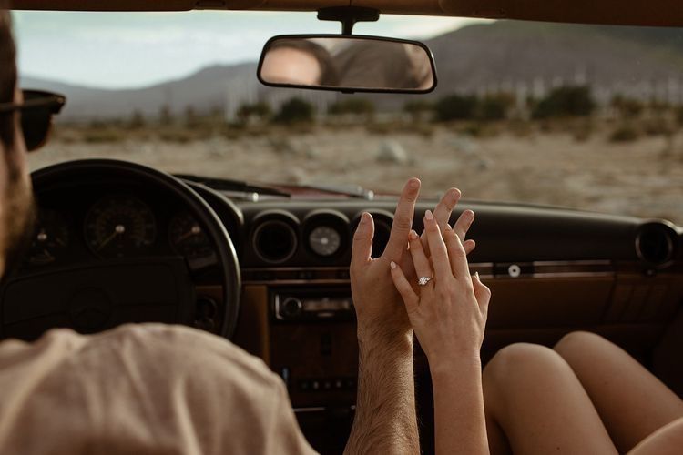 Couple holding hands in a vintage convertible car driving through a desert landscape on a romantic road trip.