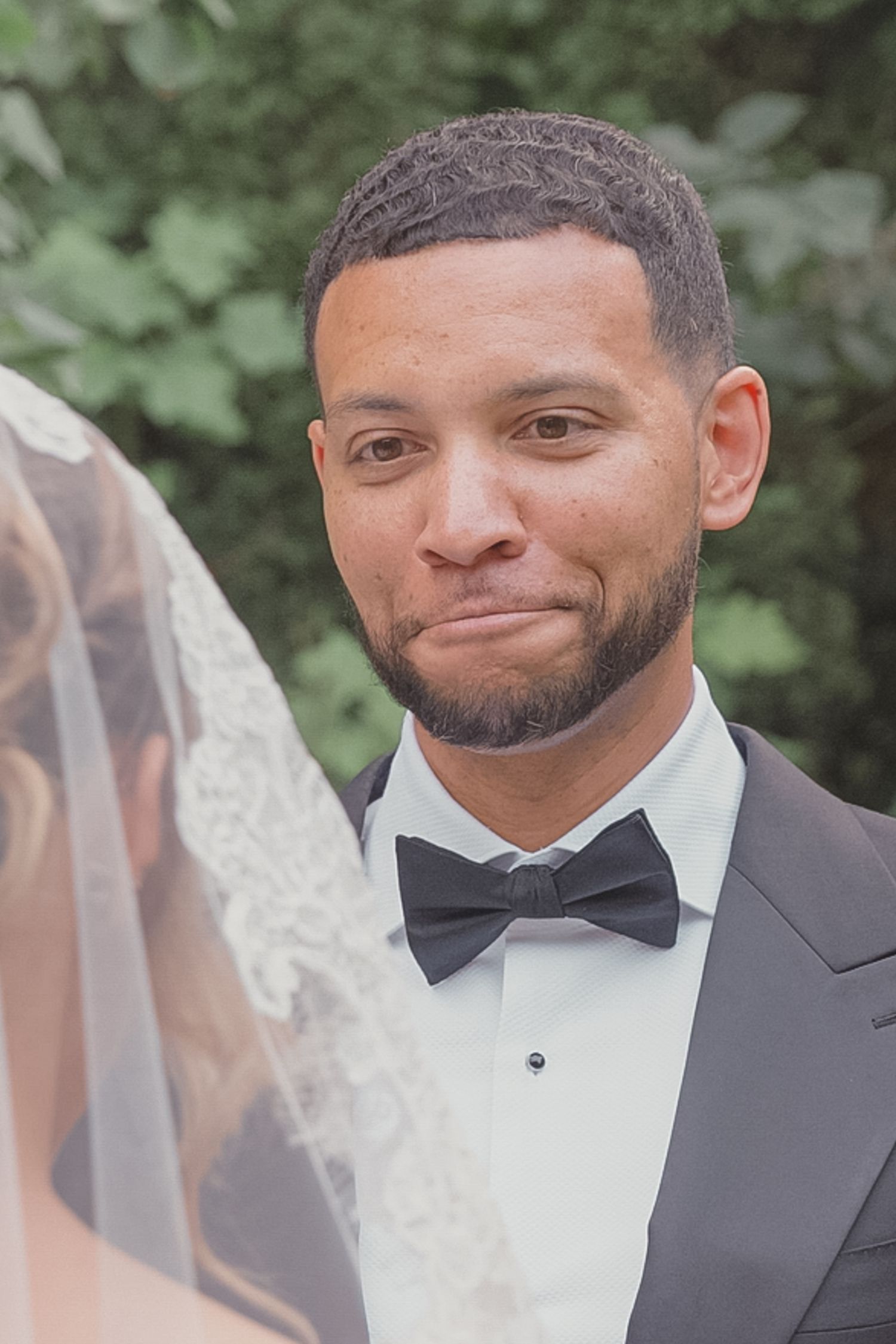 Emotional groom in black tuxedo and bow tie tearing up as he sees his bride for the first time at wedding ceremony.