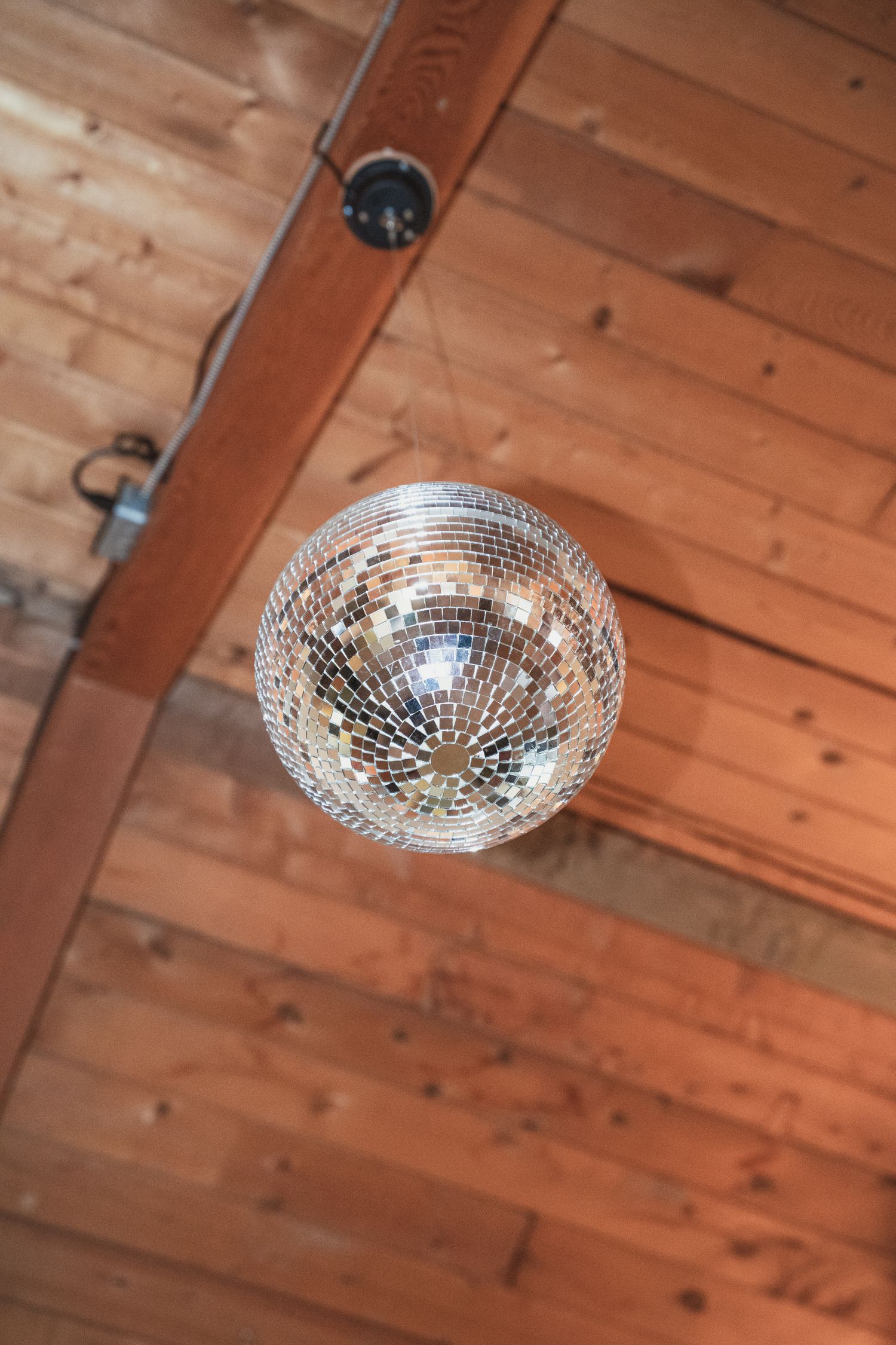 A shimmering disco ball hanging from a rustic wooden ceiling adds a festive touch to a barn wedding venue.
