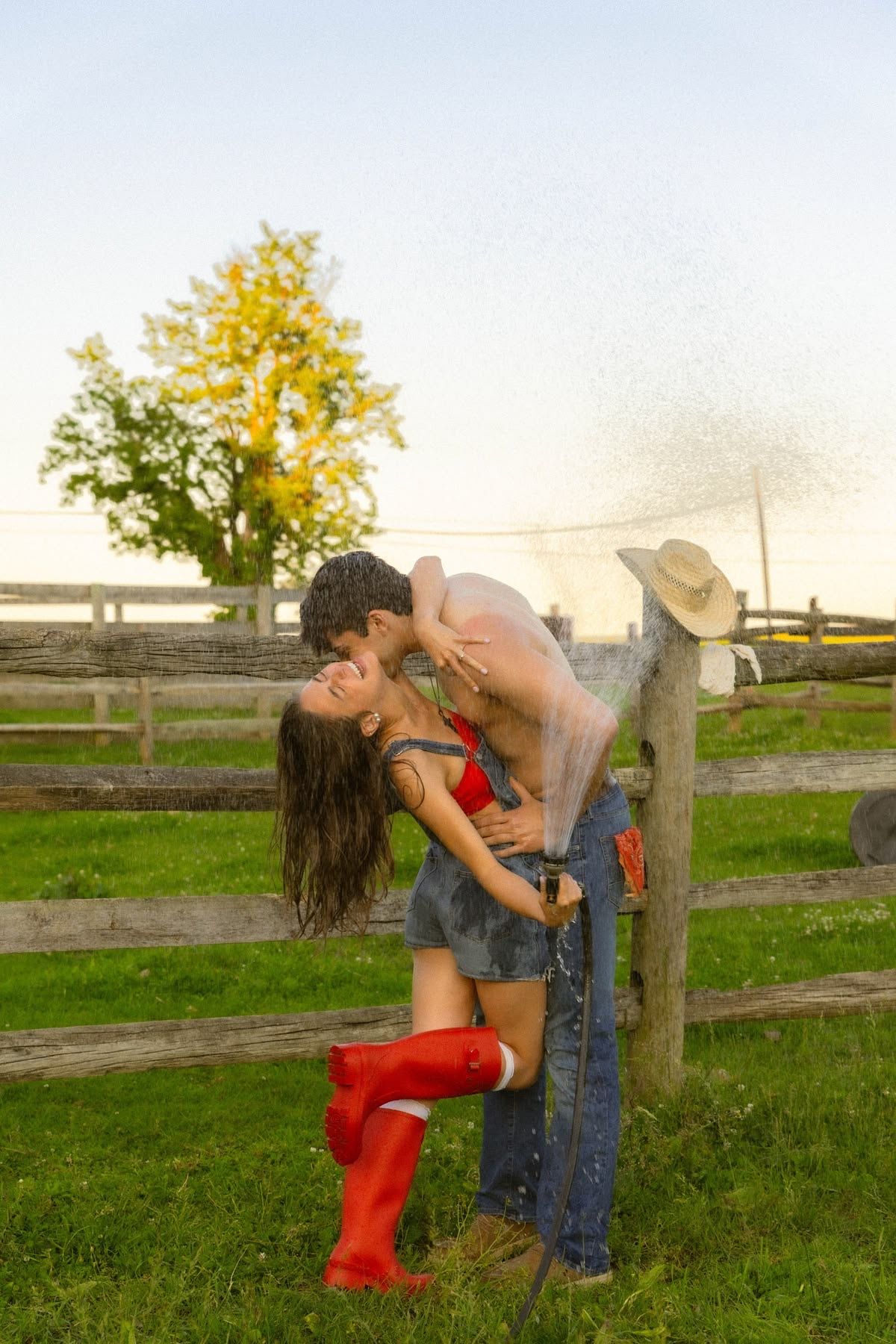 Romantic couple kissing by wooden fence on farm while being splashed with water.