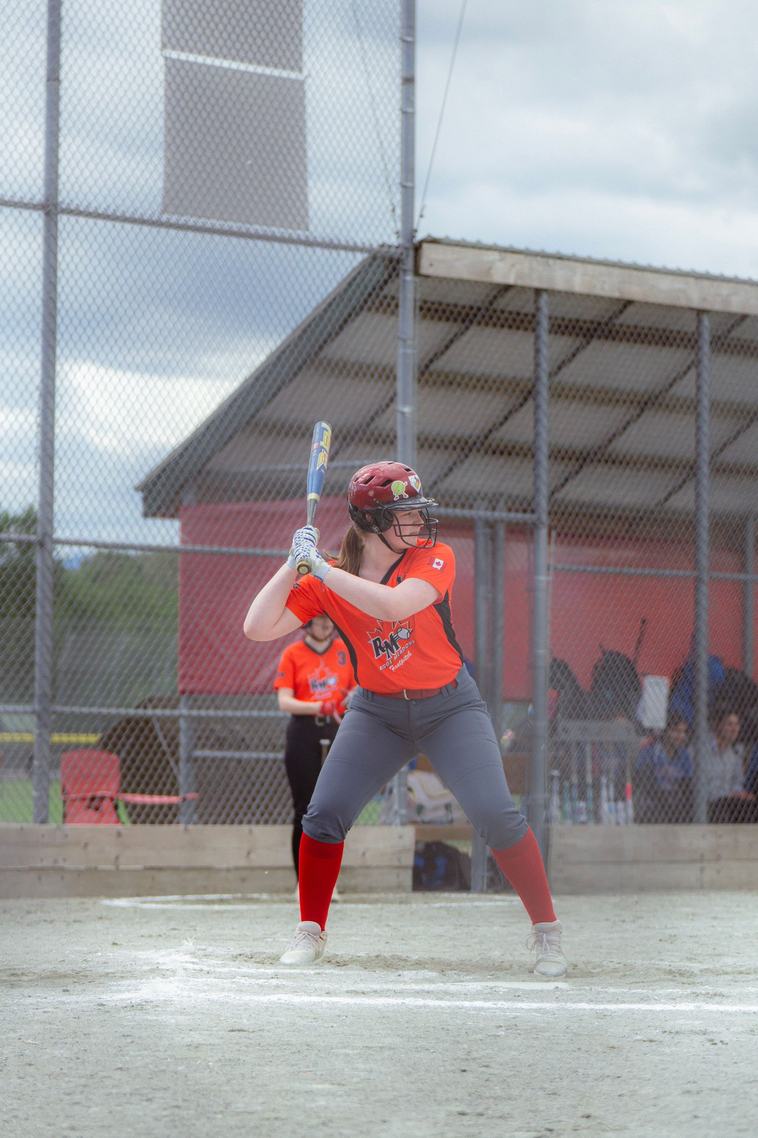 Female softball player in orange uniform prepares to bat during an outdoor softball game.