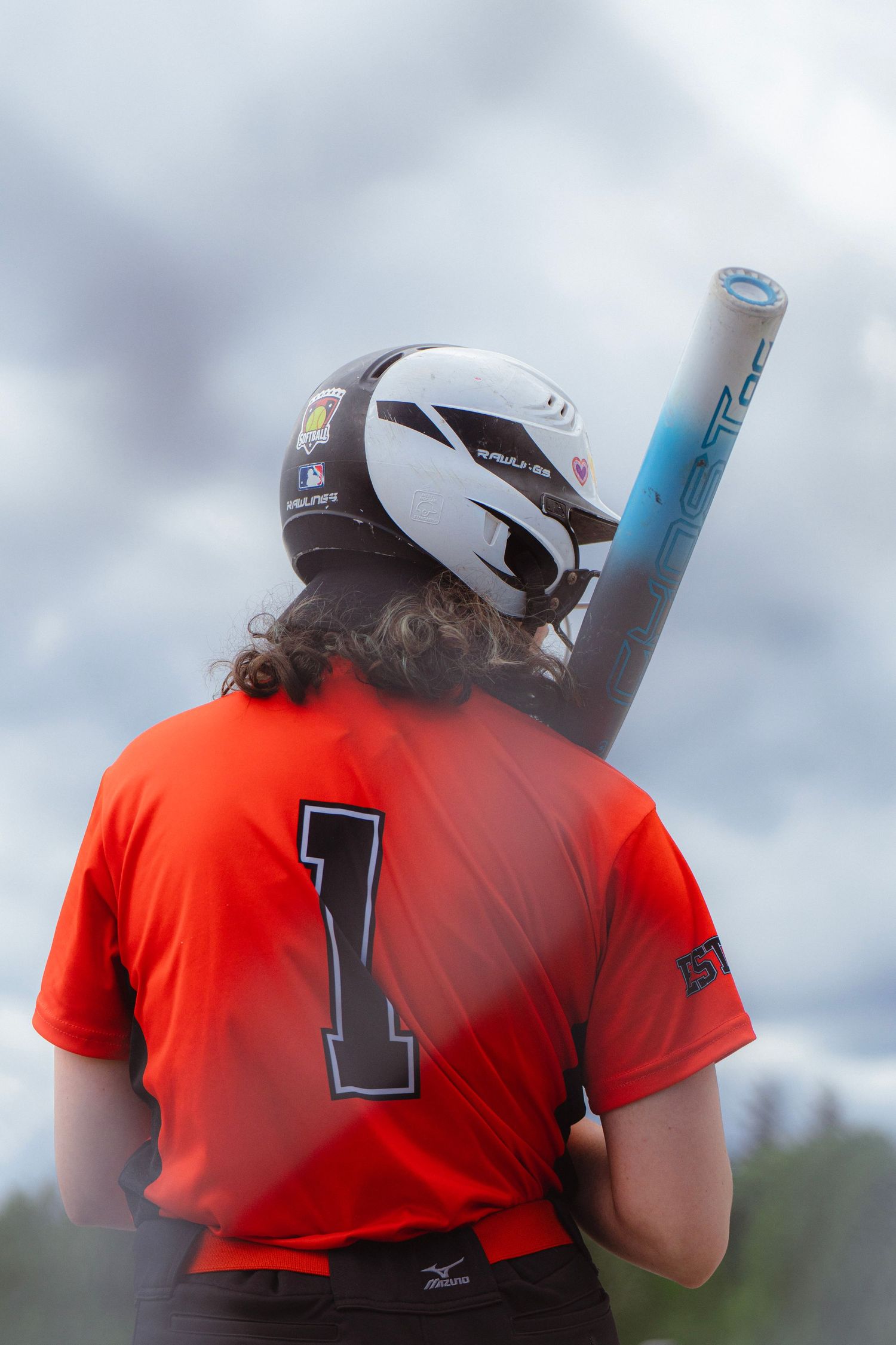 Back view of softball player number 1 in orange Mizuno jersey holding a bat over her shoulder.