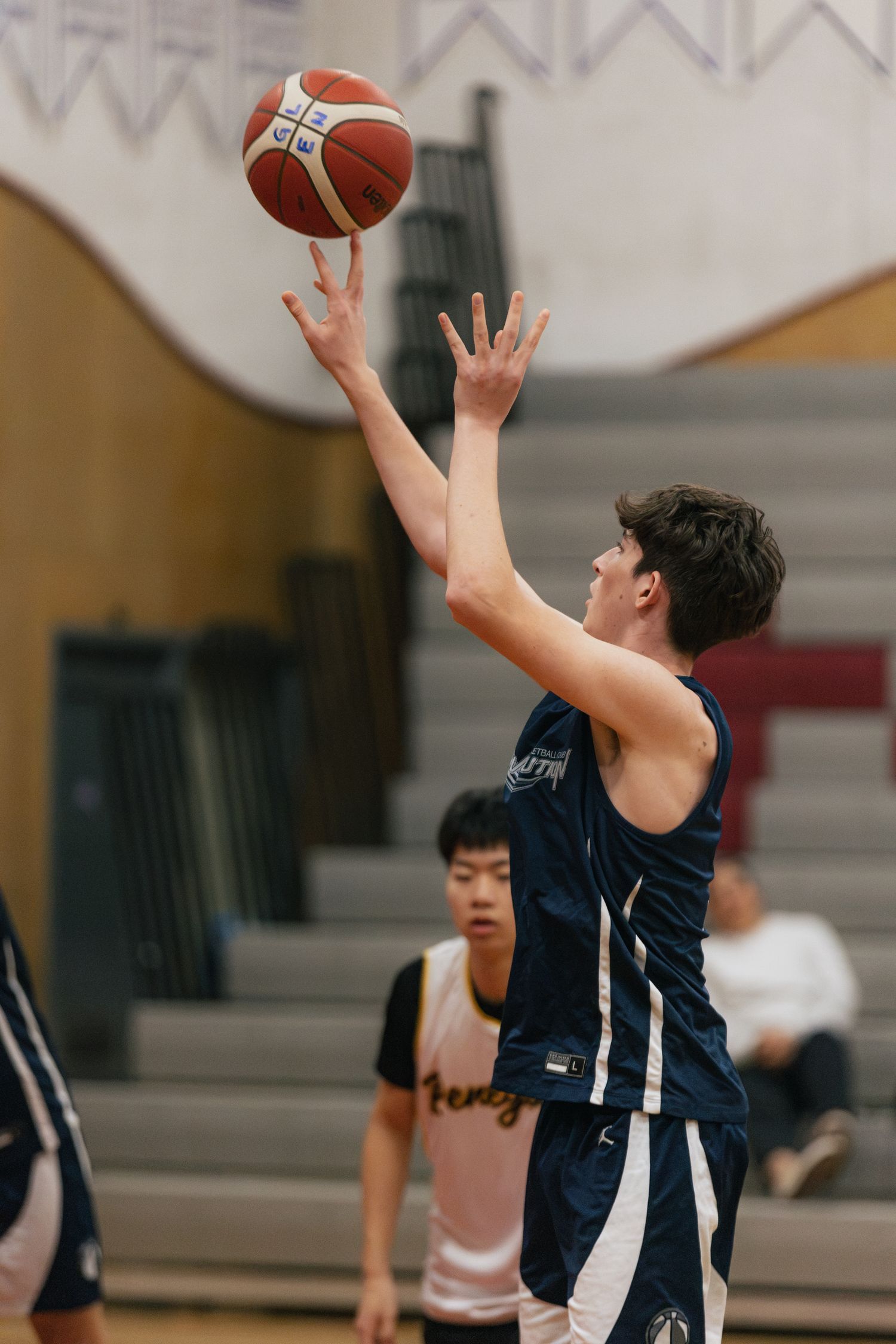 Basketball player in navy uniform releases a layup shot during an indoor gym game.