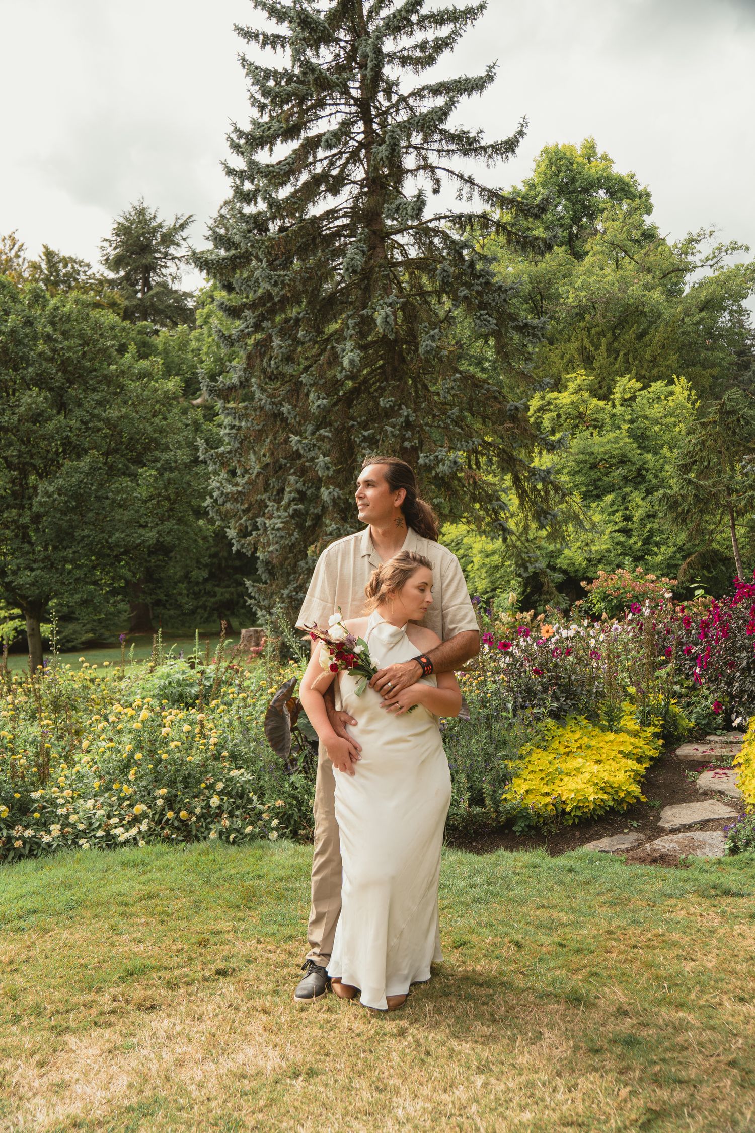Newlywed couple embracing in a vibrant garden, bride holding bouquet while groom wraps arms around her.