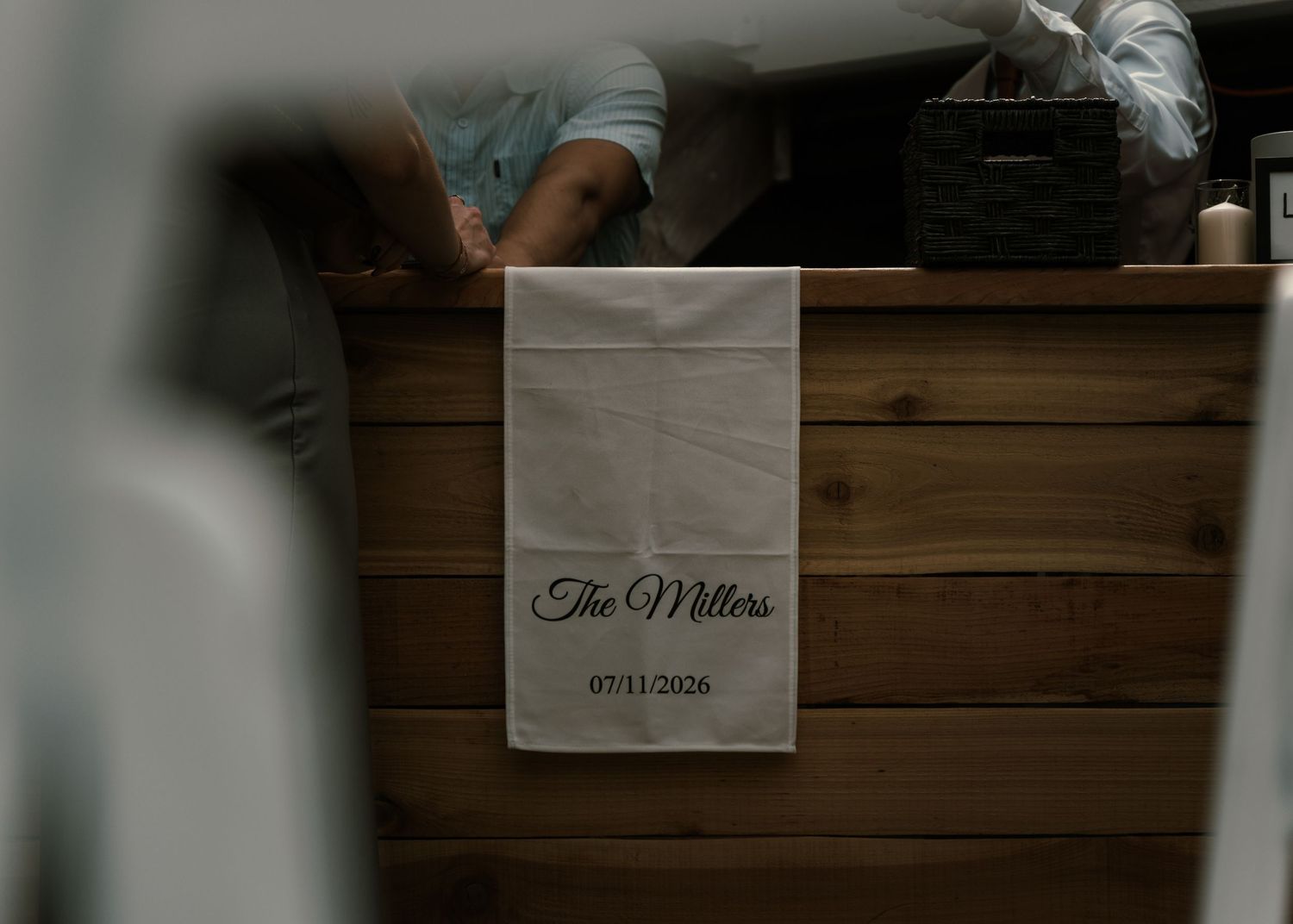 Personalized white linen table runner with The Millers wedding date 07/11/2026 displayed on rustic wooden furniture.