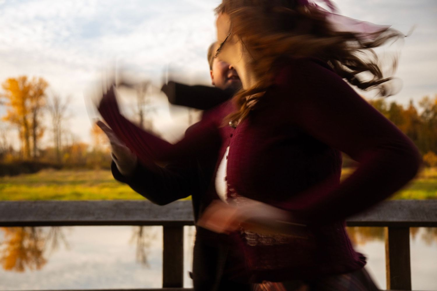 Motion blur artistic photo of couple embracing on bridge with autumn lake in background.