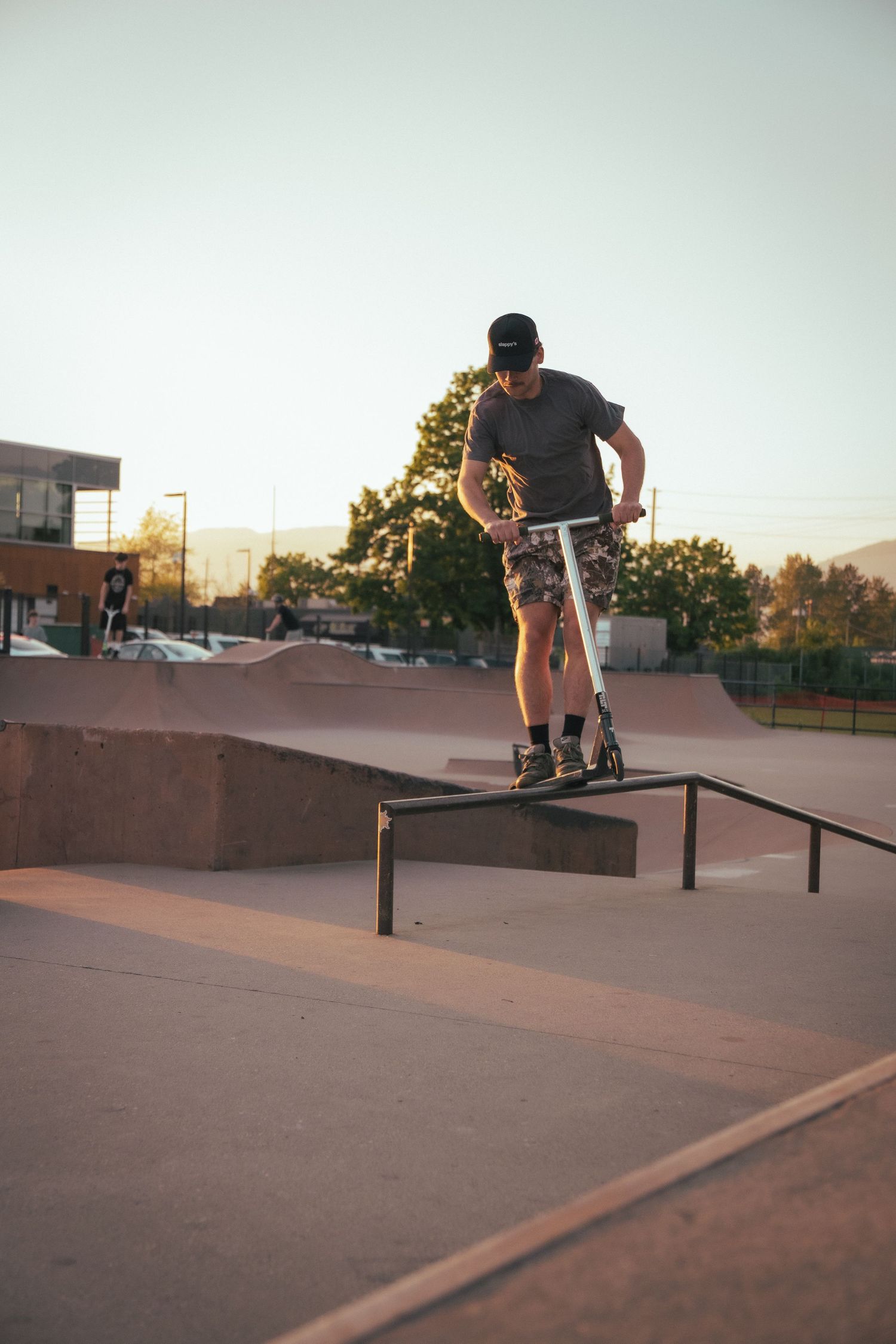 Young man performing a grind trick on a scooter over a metal rail at a skate park.