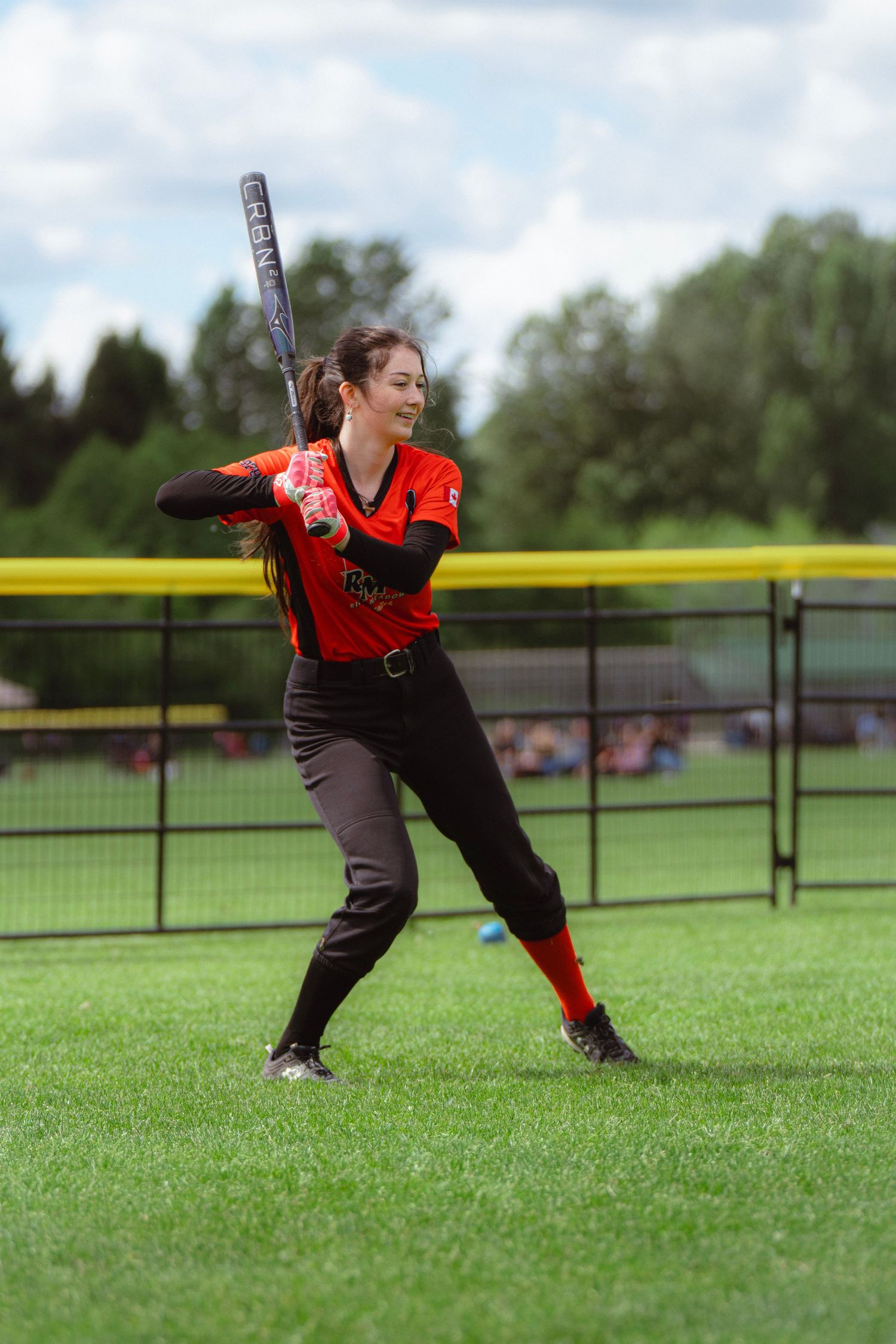 Smiling female softball player in orange jersey holding bat on field.