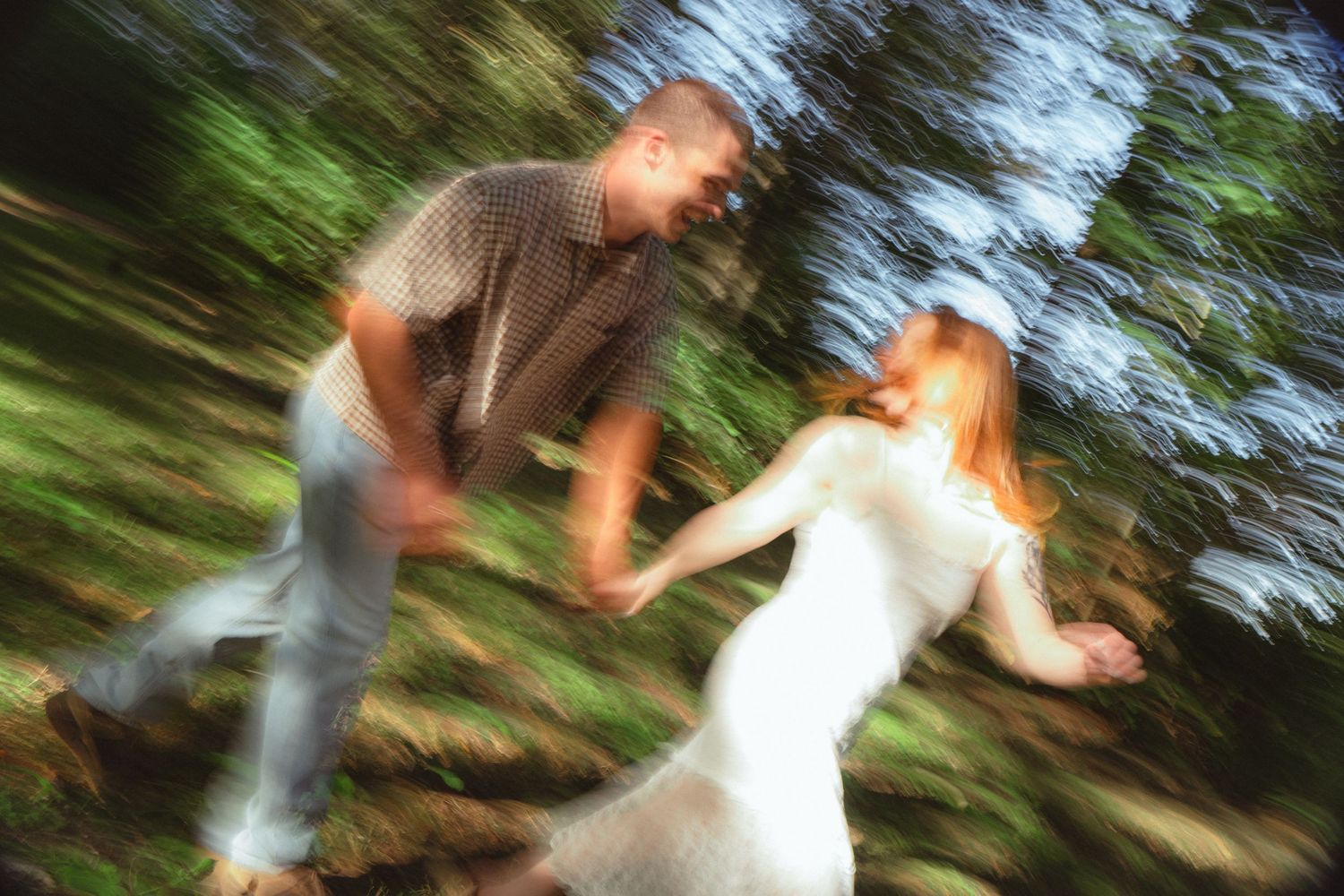Blurred motion photo of a couple dancing and spinning together in a lush green forest setting.
