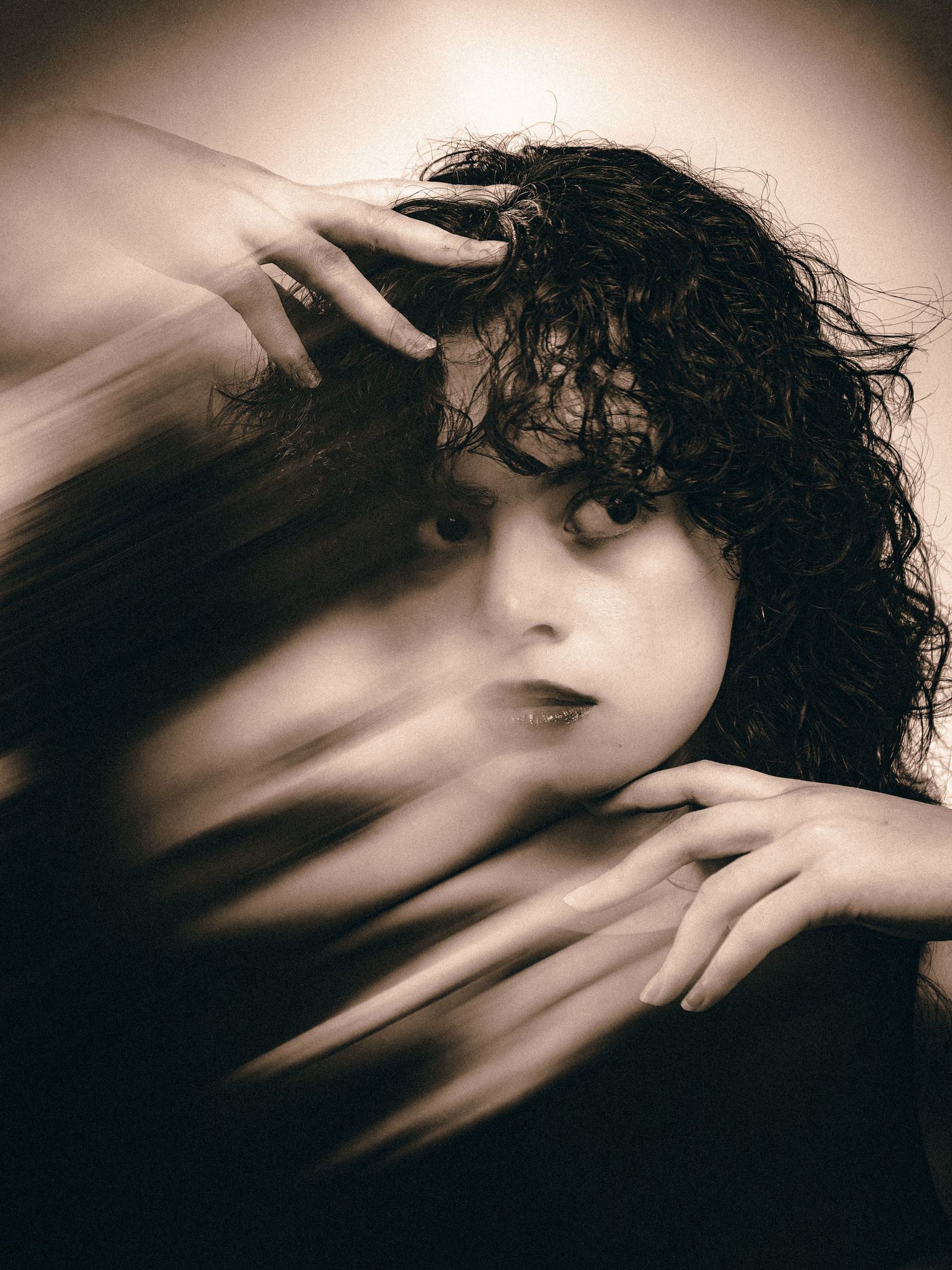Ghostly double exposure portrait of a woman with curly hair and hands reaching through a blur effect.