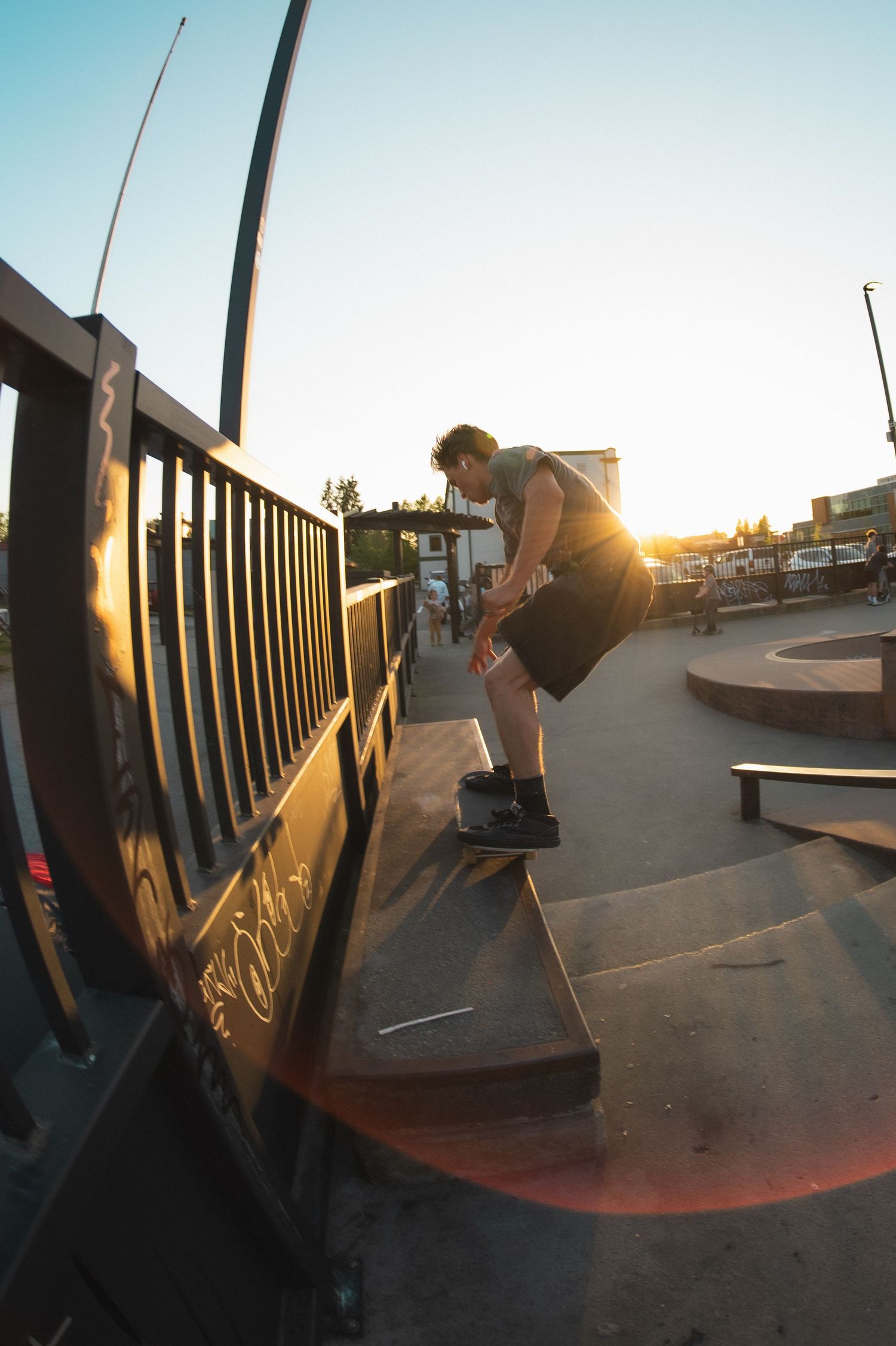 Skateboarder performing a ledge trick at an outdoor skate park bathed in golden sunset light.