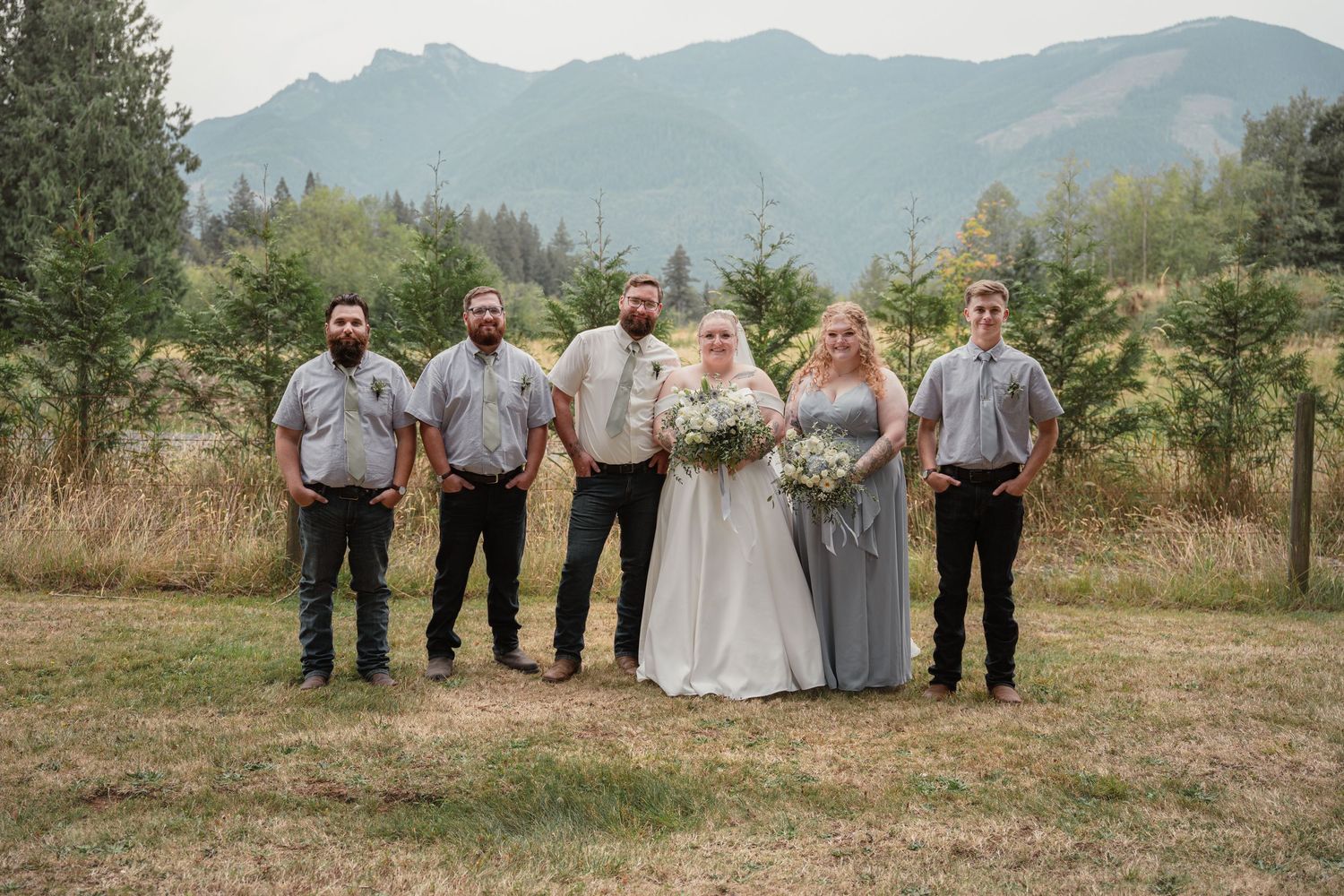 Wedding party poses in mountain meadow with bride in white gown and bridesmaids in sage.